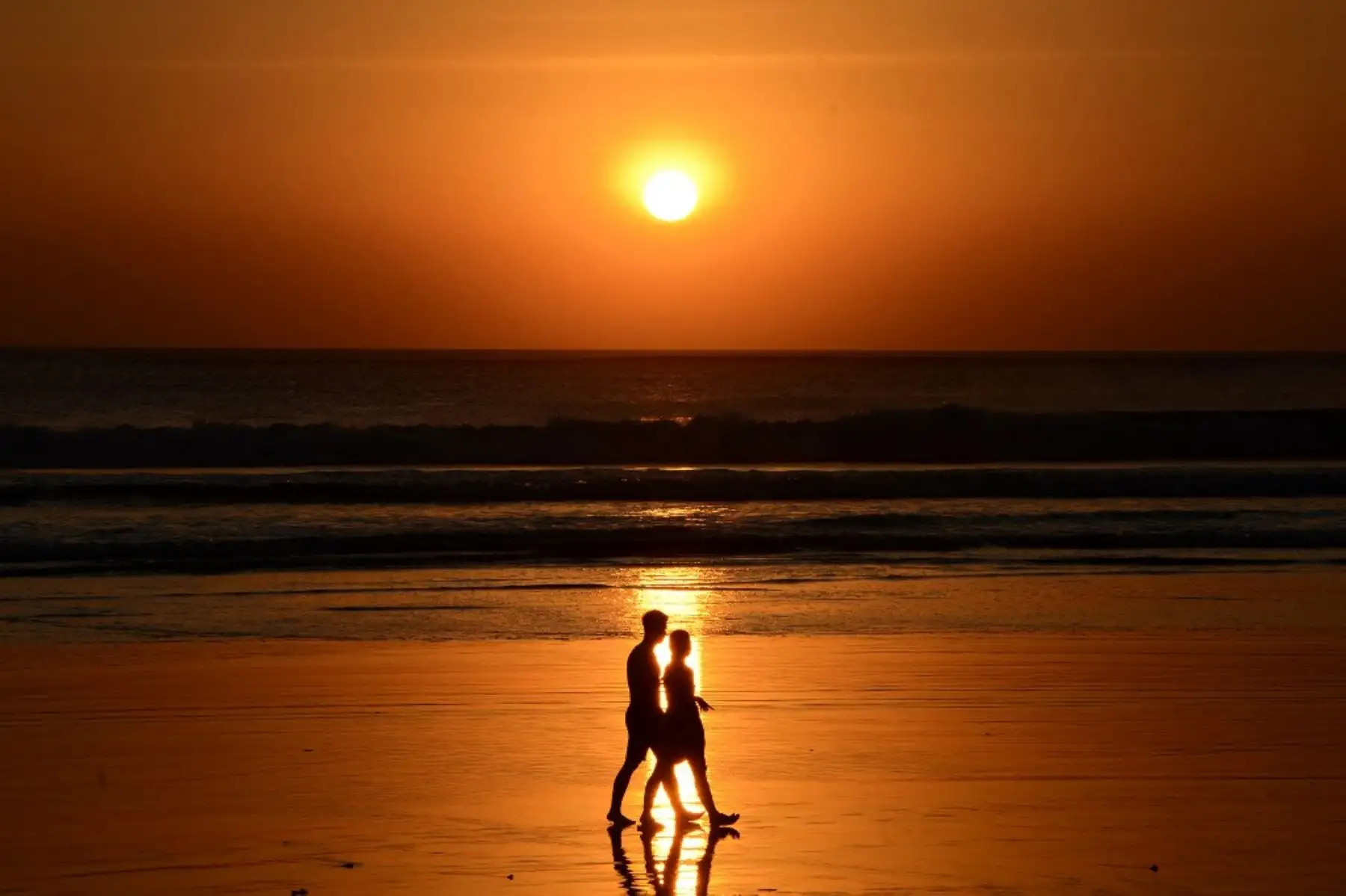 Una pareja camina durante la puesta de sol en la playa de Kuta, cerca de Denpasar, en la isla turística de Bali, Indonesia, el 11 de agosto de 2021. Foto: AFP