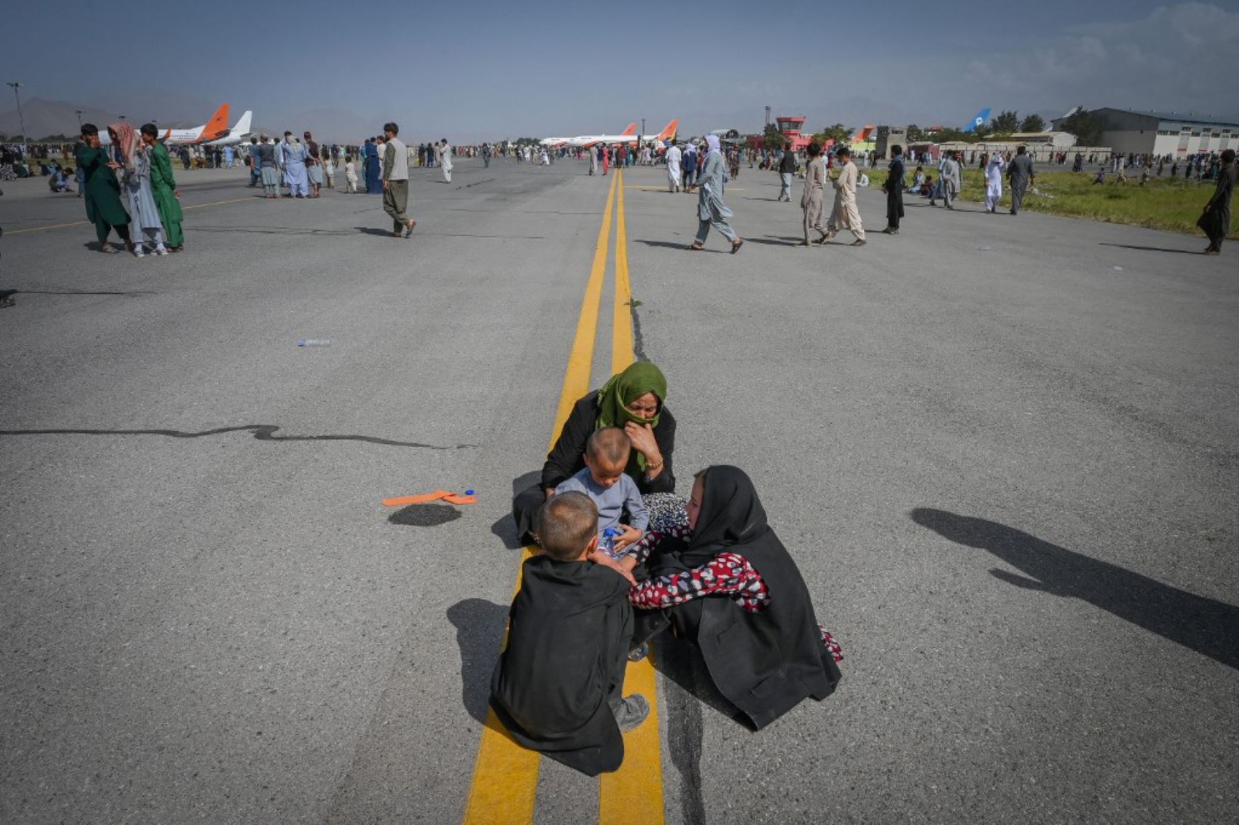 Afganos se sientan a lo largo de la pista de aterrizaje mientras esperan salir del aeropuerto de Kabul.

Foto: AFP