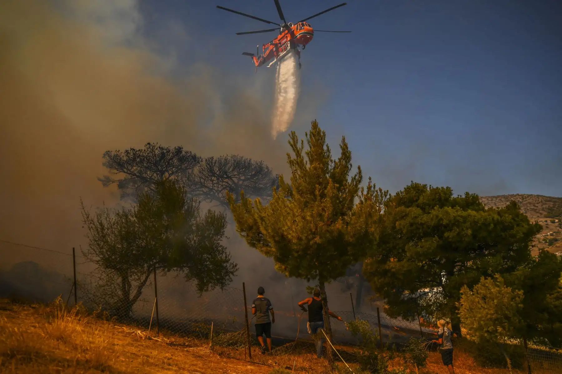 Un helicóptero arroja agua sobre las casas para extinguir el incendio en el pueblo de Markati, cerca de Atenas, Grecia. Foto: AFP