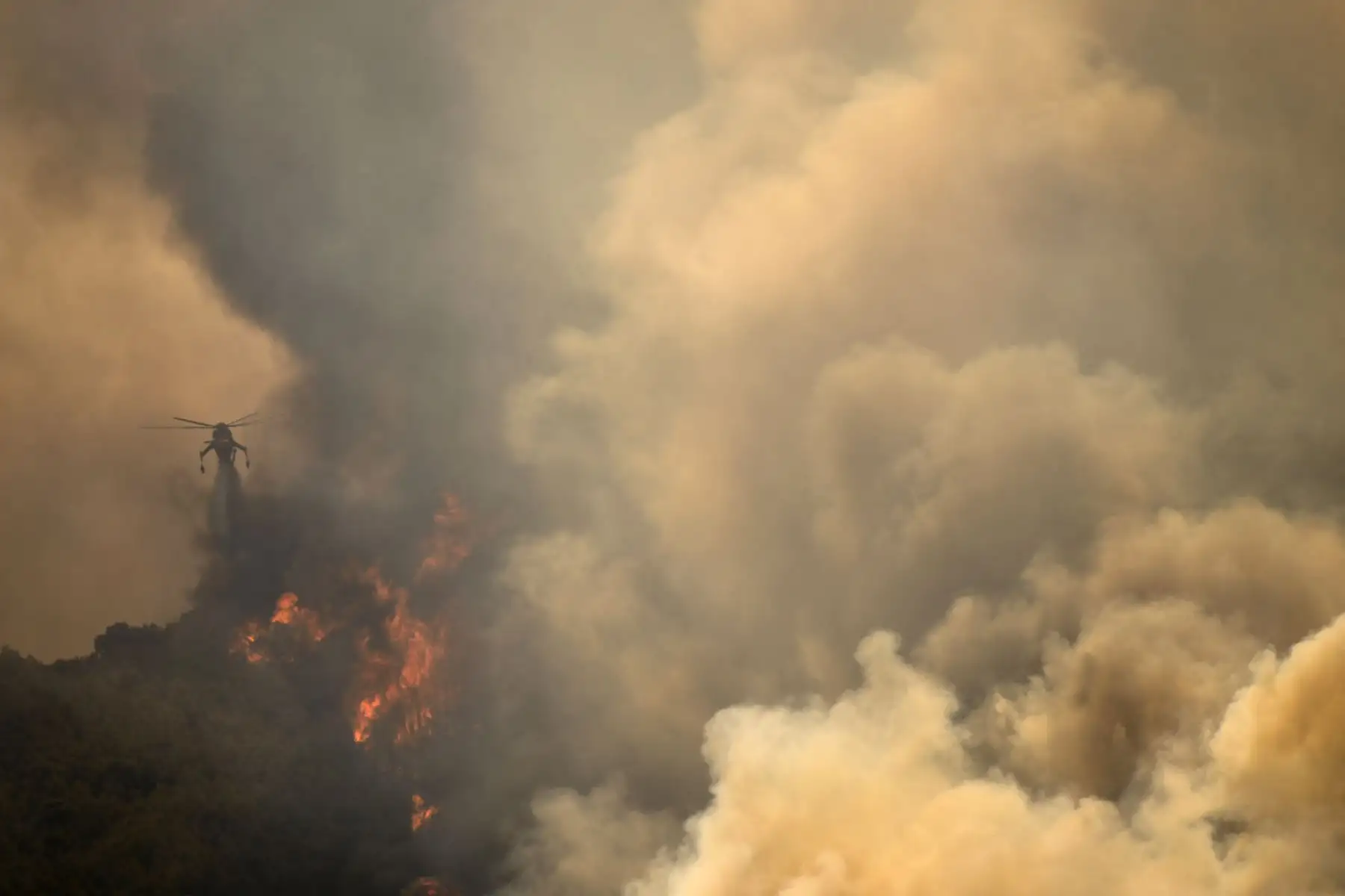 Un helicóptero arroja agua sobre las casas para extinguir el incendio en el pueblo de Markati, cerca de Atenas, Grecia. Foto: AFP