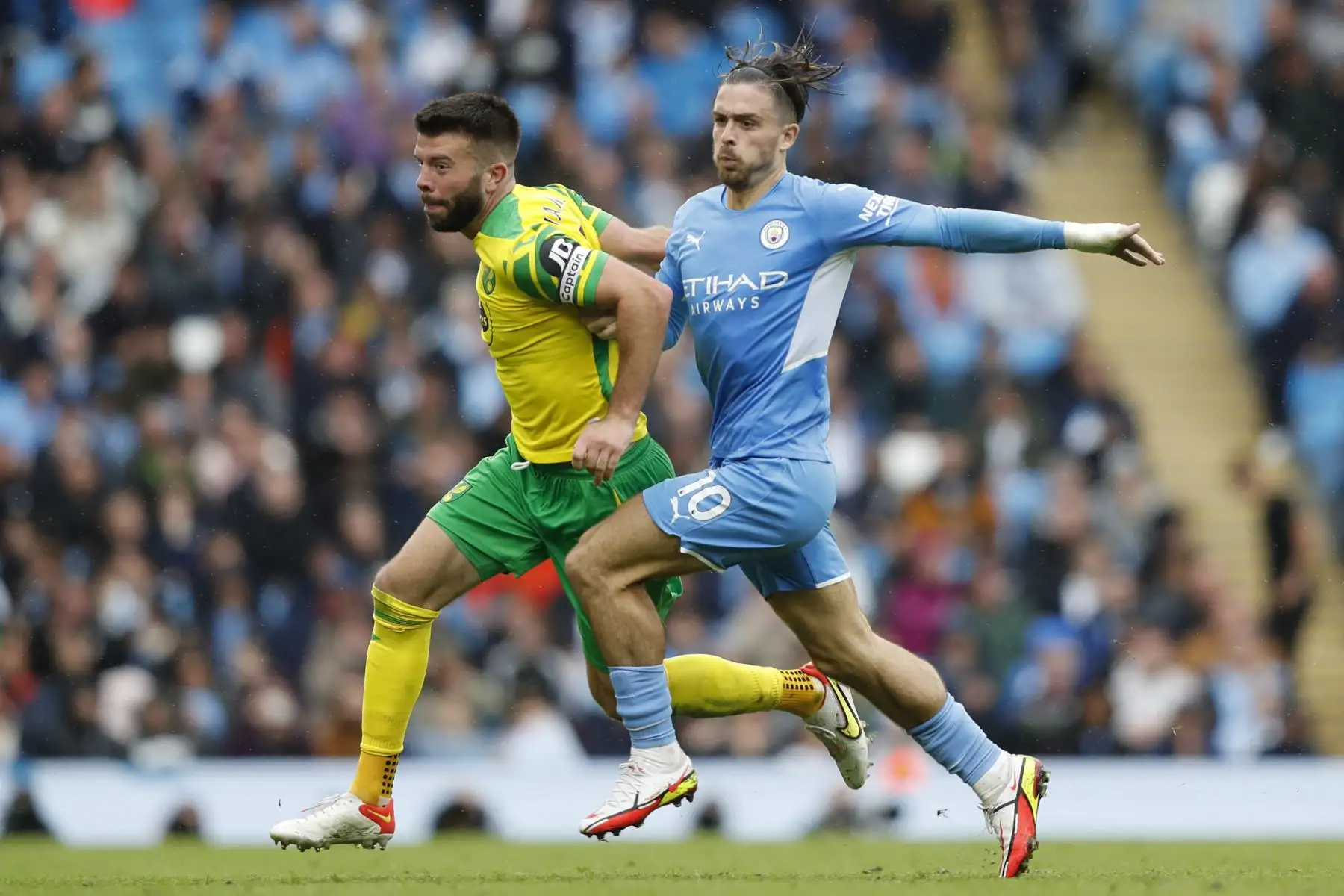 El defensor escocés del Norwich City Grant Hanley  compite con el centrocampista inglés del Manchester City Jack Grealish durante el partido de fútbol de la Premier League, en el Etihad Stadium de Manchester. Foto: AFP