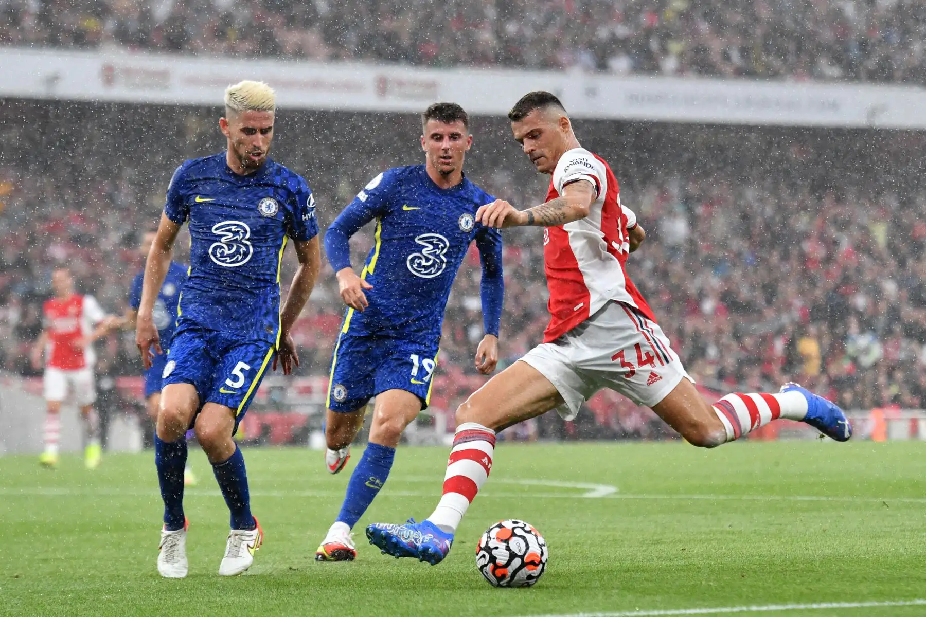 El centrocampista suizo del Arsenal Granit Xhaka se prepara para cruzar el balón ante la marca del centrocampista italiano Jorginho y el inglés Mason Mount del Chelsea durante partido de la Premier League, en el Emirates Stadium de Londres. Foto: AFP