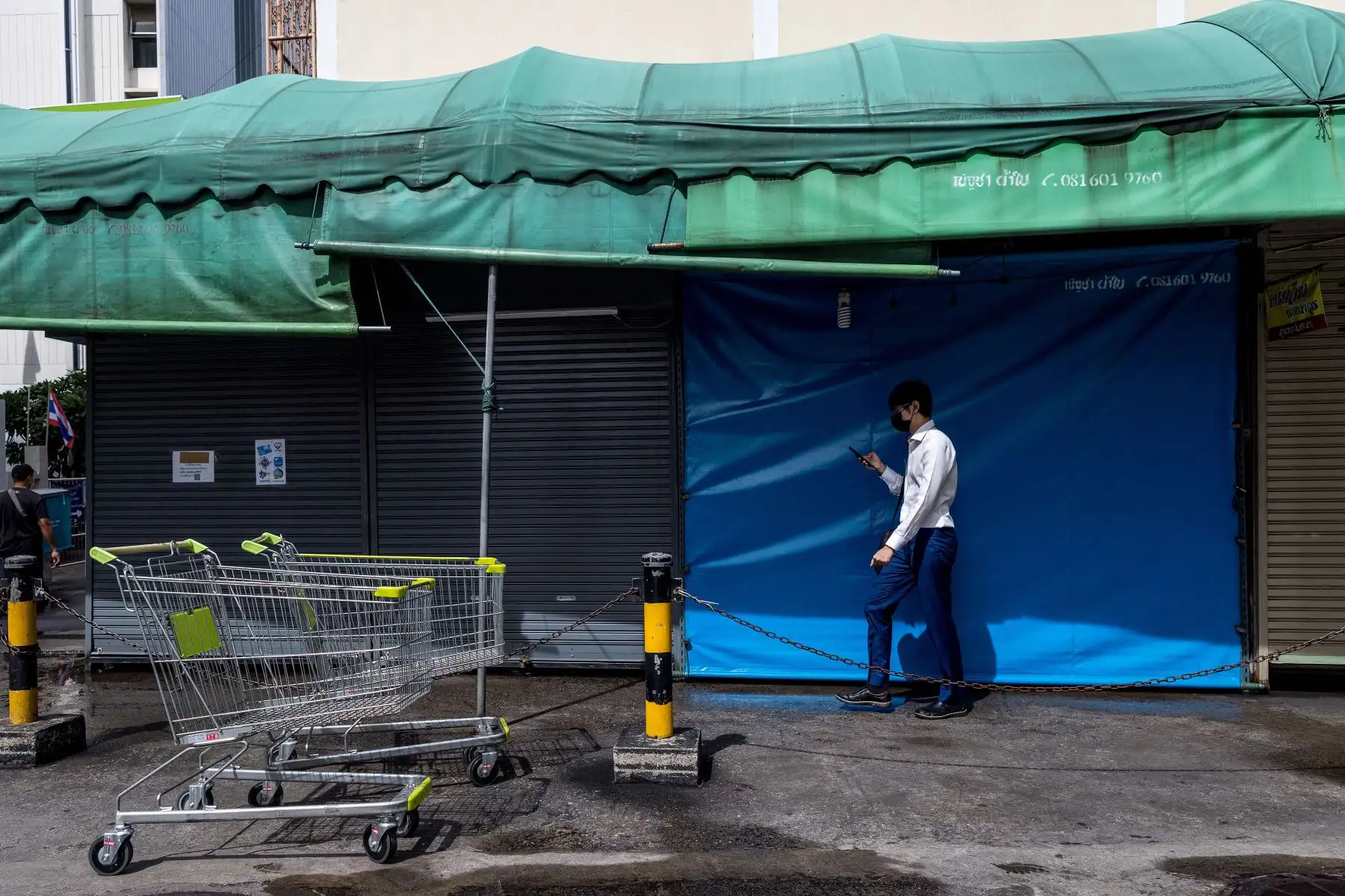 Un hombre revisa su teléfono mientras pasa por puestos de mercado cerrados en Bangkok, antes de la relajación de algunas de las restricciones del coronavirus  en Tailandia.
Foto: AFP