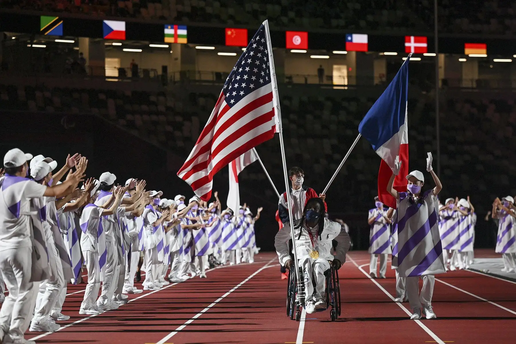 Las banderas de Estados Unidos (anverso) y Francia (reverso) se llevan durante la ceremonia de clausura de los Juegos Paralímpicos de Tokio 2020 en el Estadio Olímpico. Foto: AFP