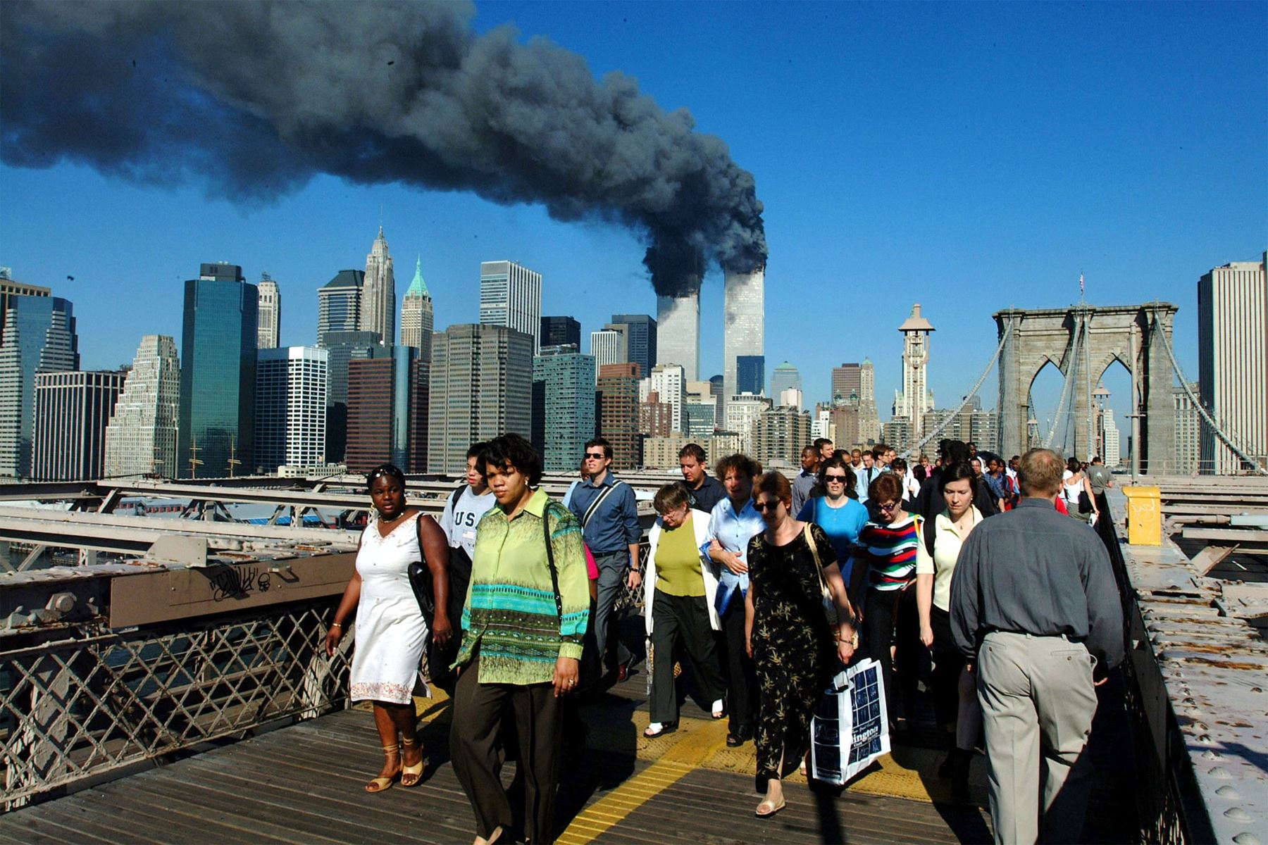 Los peatones cruzan el Puente de Brooklyn alejándose de las torres de World Trade en llamas antes de su derrumbe el 11 de septiembre de 2001. Ambas torres fueron alcanzadas por aviones de pasajeros secuestrados en un  ataque terrorista. Ambas torres colapsaron más tarde. 
Foto: AFP