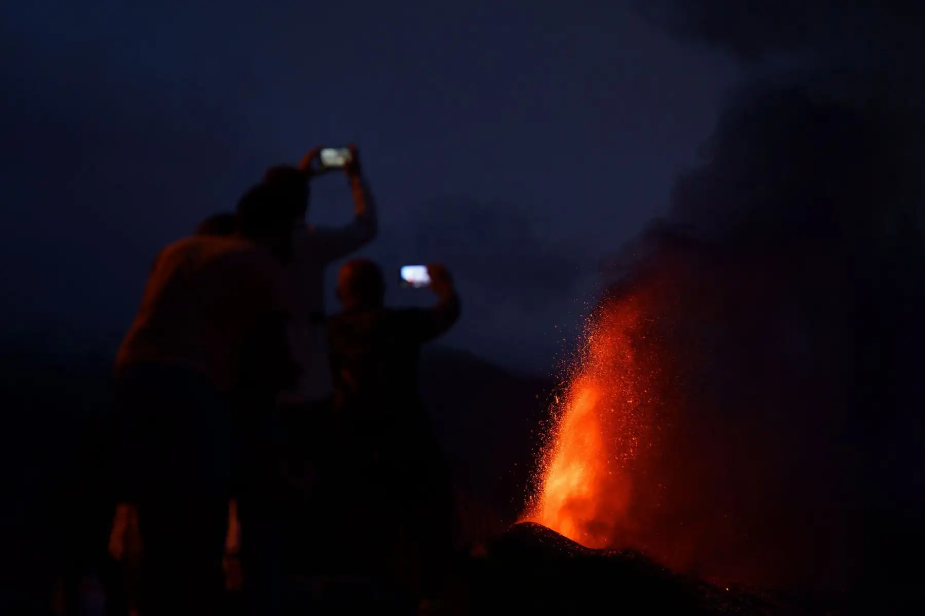 Cuatro personas contemplan desde una montaña al caer la noche la lava que sale proyectada hacia el cielo del nuevo volcán de La Palma.
Foto: EFE