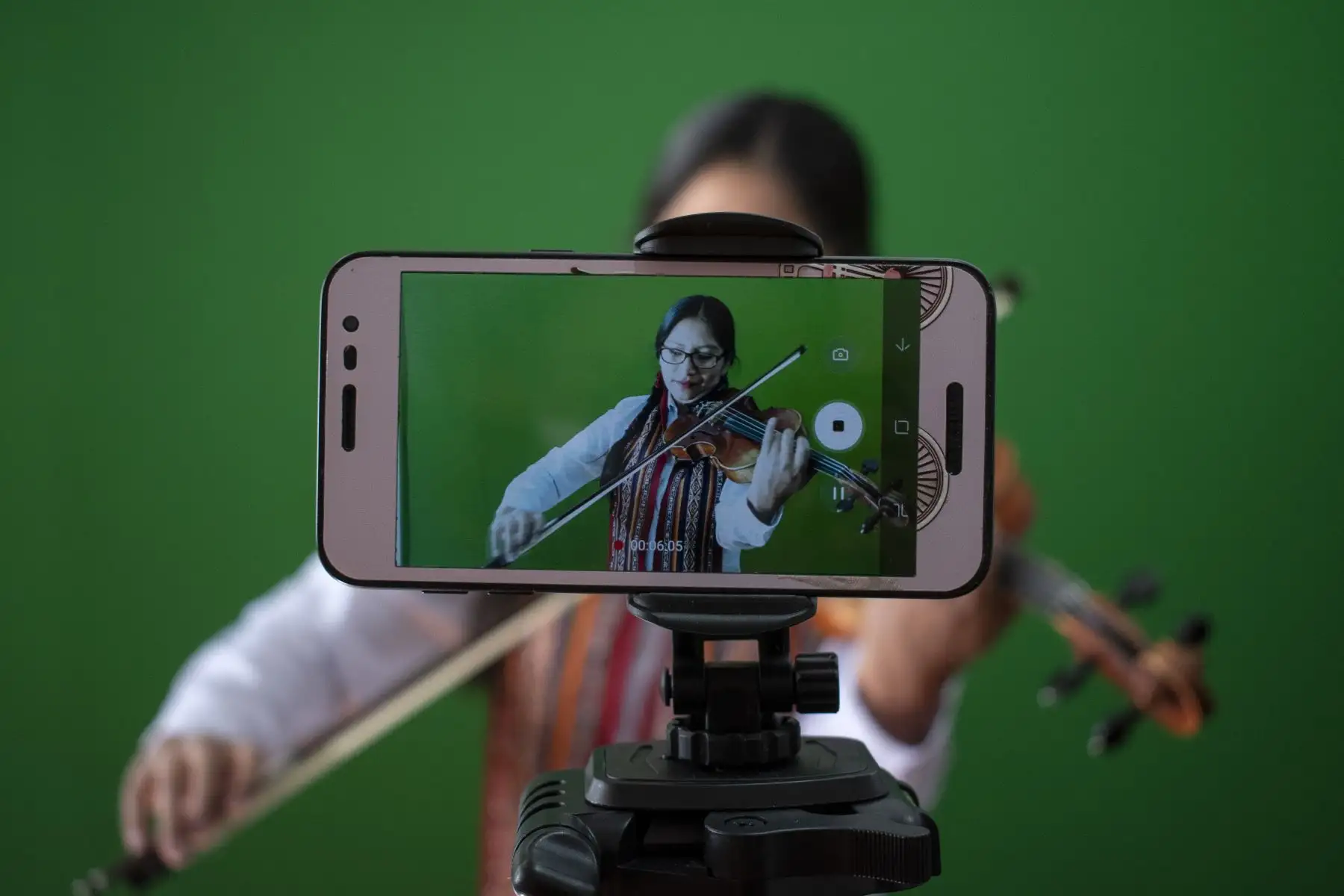 Desde el inicio de la cuarentena, la Orquesta Sinfónica del Cusco presenta semanalmente conciertos virtuales temáticos que difunden la música tradicional-académica. Cada integrante ha sido capacitado para grabar los videos desde casa. En la foto, la violinista Doris Quispe se graba con su celular. Foto: Sharon Castellanos, con el apoyo del Fondo de emergencia COVID-19 de The National Geographic Society