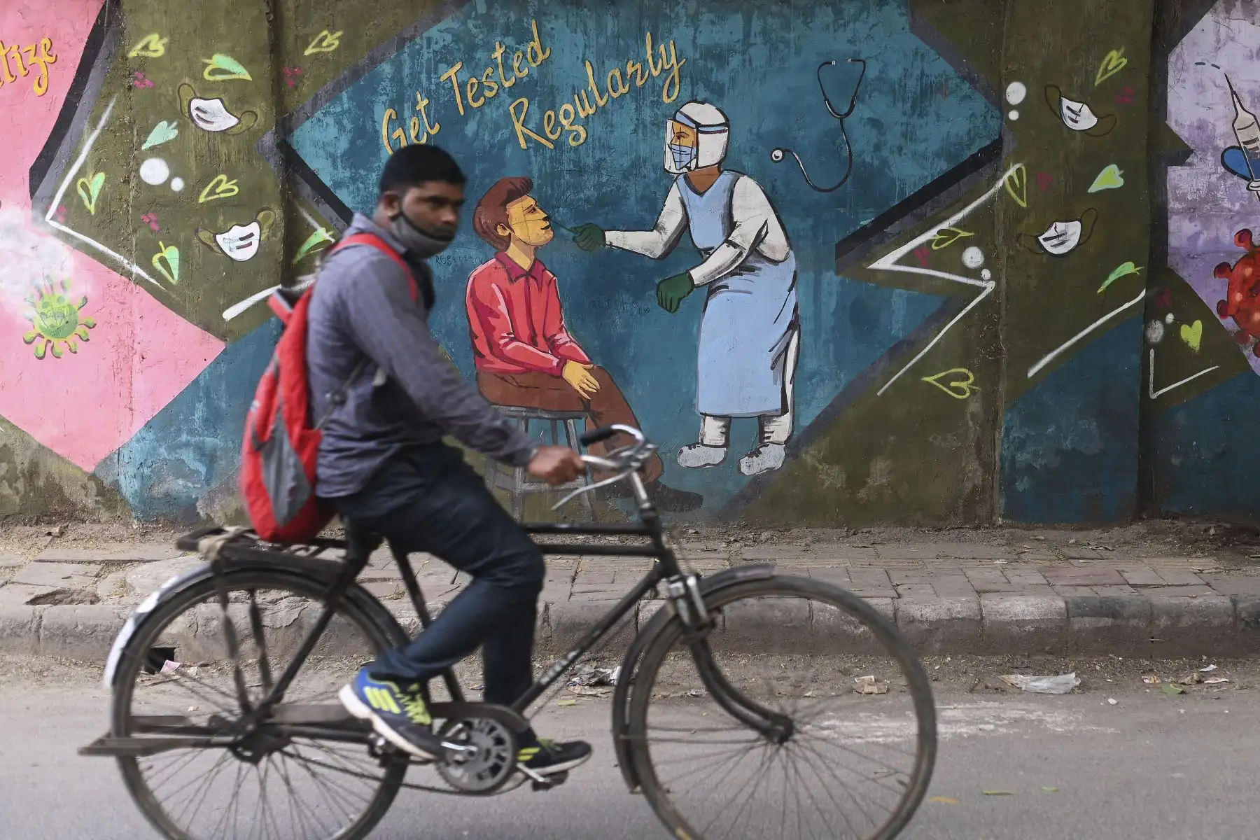 Un ciclista pasa junto a un mural que muestra a un trabajador de la salud que realiza pruebas de coronavirus covid-19 en Nueva Delhi.
Foto: AFP