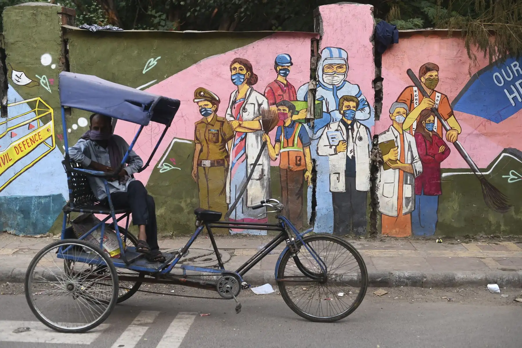 Un conductor de rickshaw espera a los clientes frente a un mural que muestra a los trabajadores de primera línea del coronavirus covid-19 en Nueva Delhi.
Foto: AFP