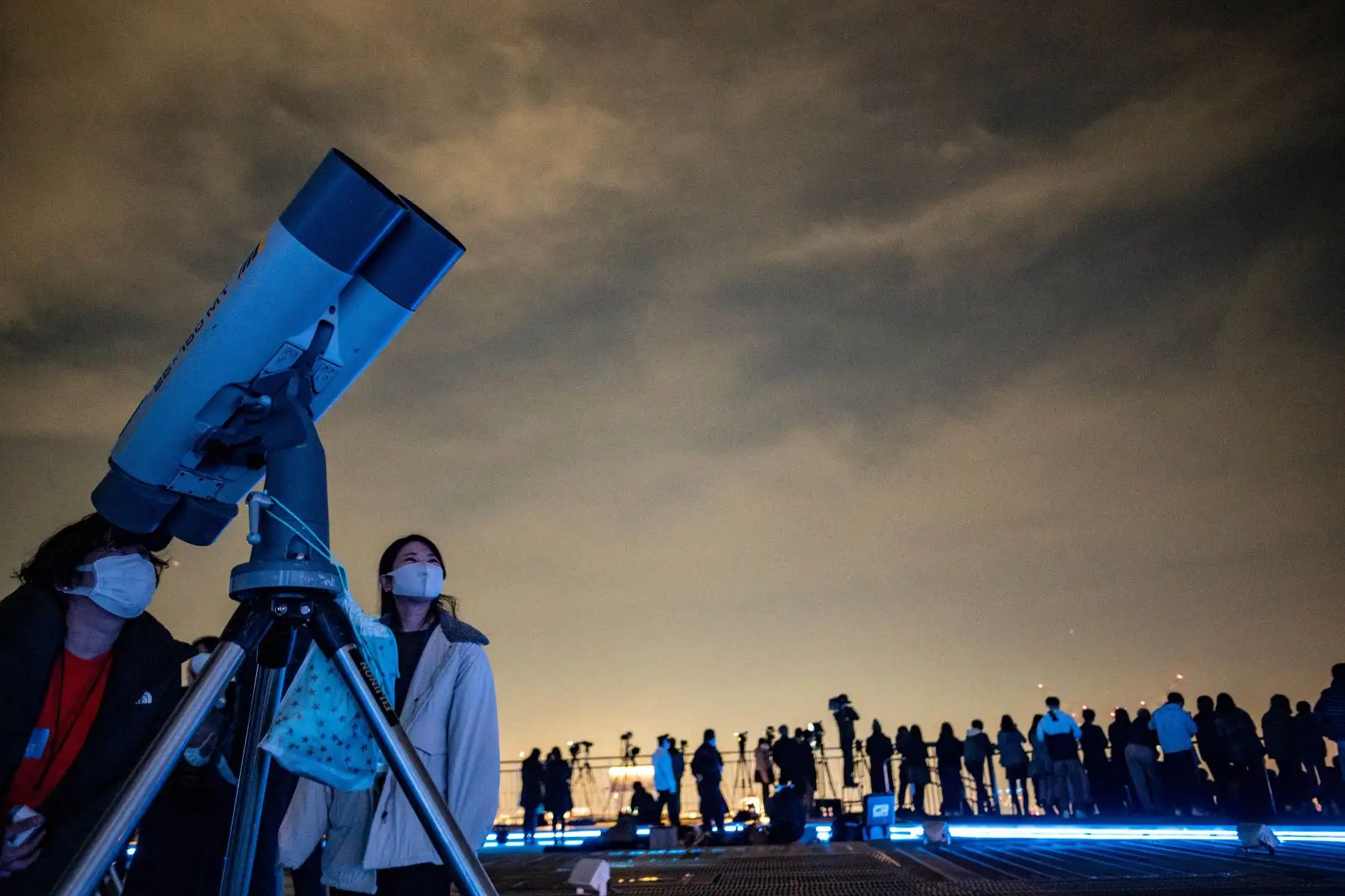La gente observa el cielo nocturno con un telescopio mientras fotógrafos y videoperiodistas documentan un eclipse lunar desde la plataforma de observación de Roppongi Hills en Tokio. Foto: AFP