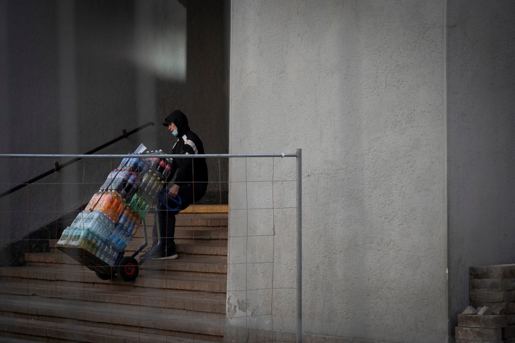 Un hombre con una mascarilla levanta un carrito cargado con agua embotellada y otras bebidas por las escaleras en Moscú. Foto: AFP