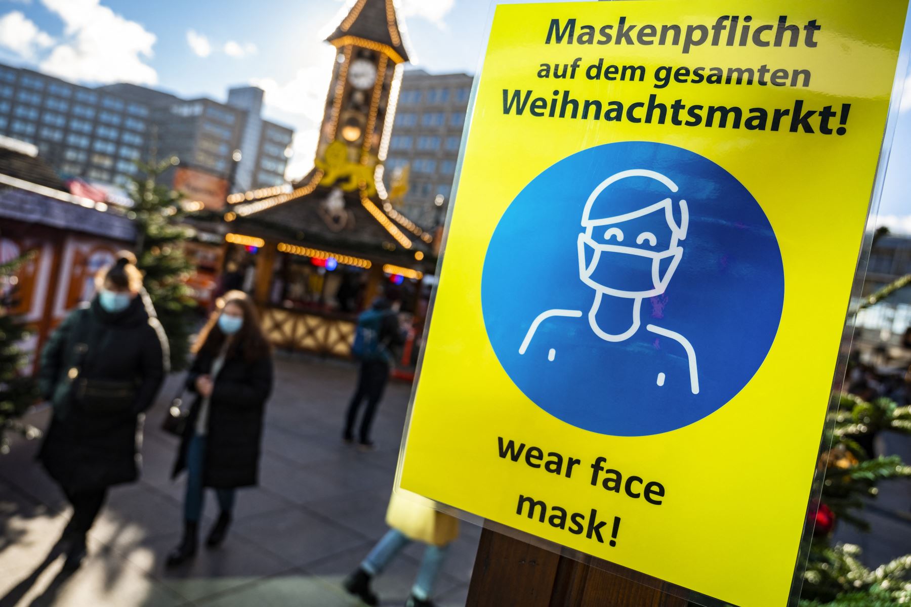 Un letrero que solicita a los visitantes que usen máscaras protectoras se ve cerca de ambos en un mercado navideño en Alexanderplatz en Berlín. Foto: AFP