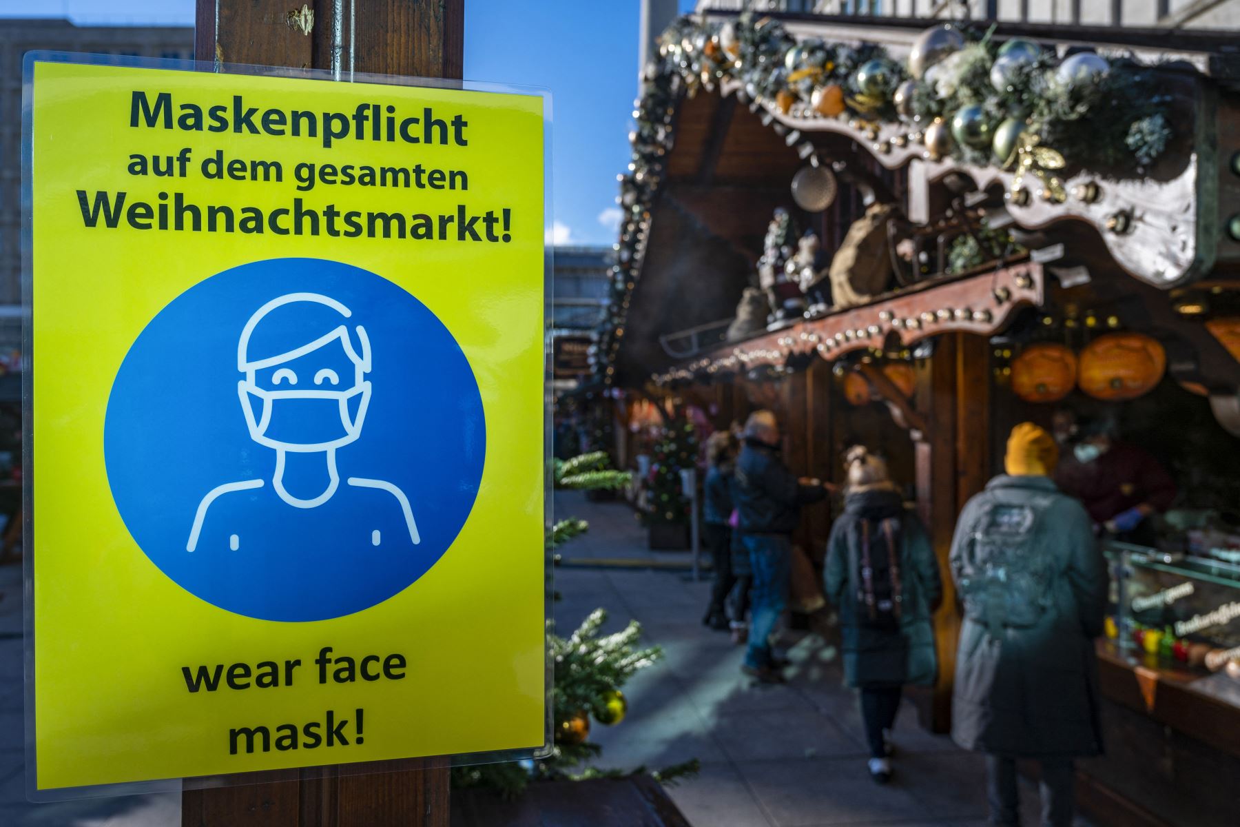 Un letrero que solicita a los visitantes que usen máscaras protectoras se ve cerca de ambos en un mercado navideño en Alexanderplatz en Berlín. Foto: AFP