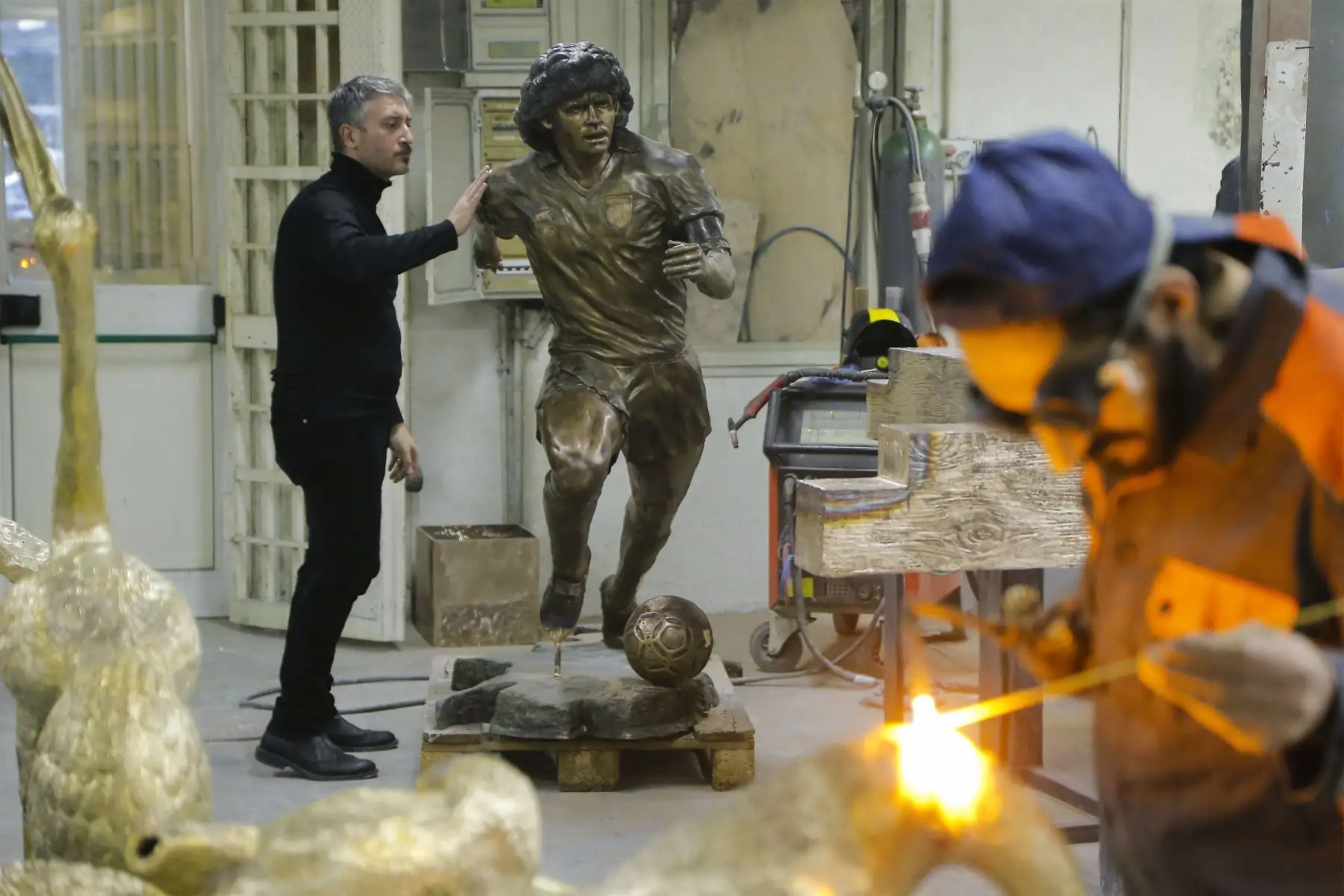 Un soldador trabaja  mientras el escultor italiano Domenico Sepe toca una estatua de bronce de tamaño natural del fallecido leyenda del fútbol argentino Diego Armando Maradona,  en su estudio en Nápoles. 
Foto: AFP