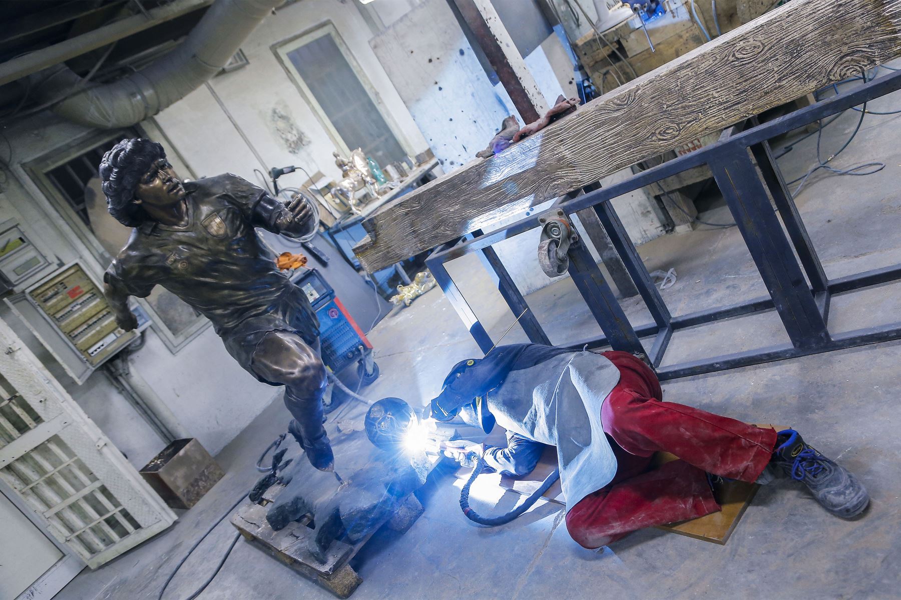 Un soldador trabaja  mientras el escultor italiano Domenico Sepe toca una estatua de bronce de tamaño natural del fallecido leyenda del fútbol argentino Diego Armando Maradona,  en su estudio en Nápoles. 
Foto: AFP