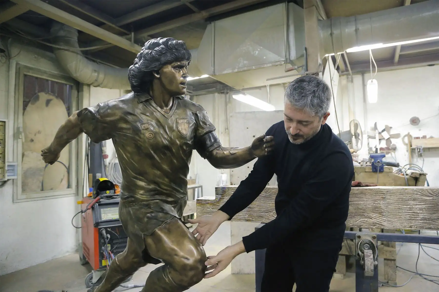 Un soldador trabaja  mientras el escultor italiano Domenico Sepe toca una estatua de bronce de tamaño natural del fallecido leyenda del fútbol argentino Diego Armando Maradona,  en su estudio en Nápoles. 
Foto: AFP