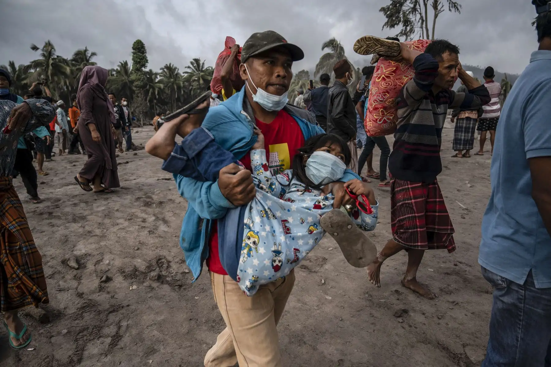 Un aldeano carga a un niño mientras los demás llevan consigo sus pertenencias en un área cubierta de ceniza volcánica, en la aldea de Sumber Wuluh, en Lumajang, Indonesia. Foto: AFP
