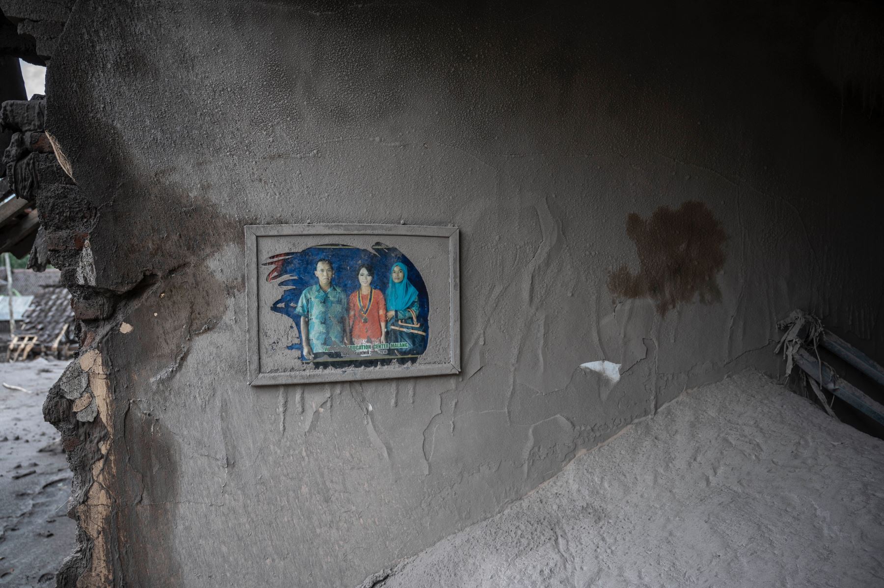 Un retrato familiar todavía cuelga en una casa dañada en la aldea de Sumber Wuluh en Lumajang el 6 de diciembre de 2021, luego de una erupción volcánica del Monte Semeru que mató al menos a catorce personas. Foto: AFP