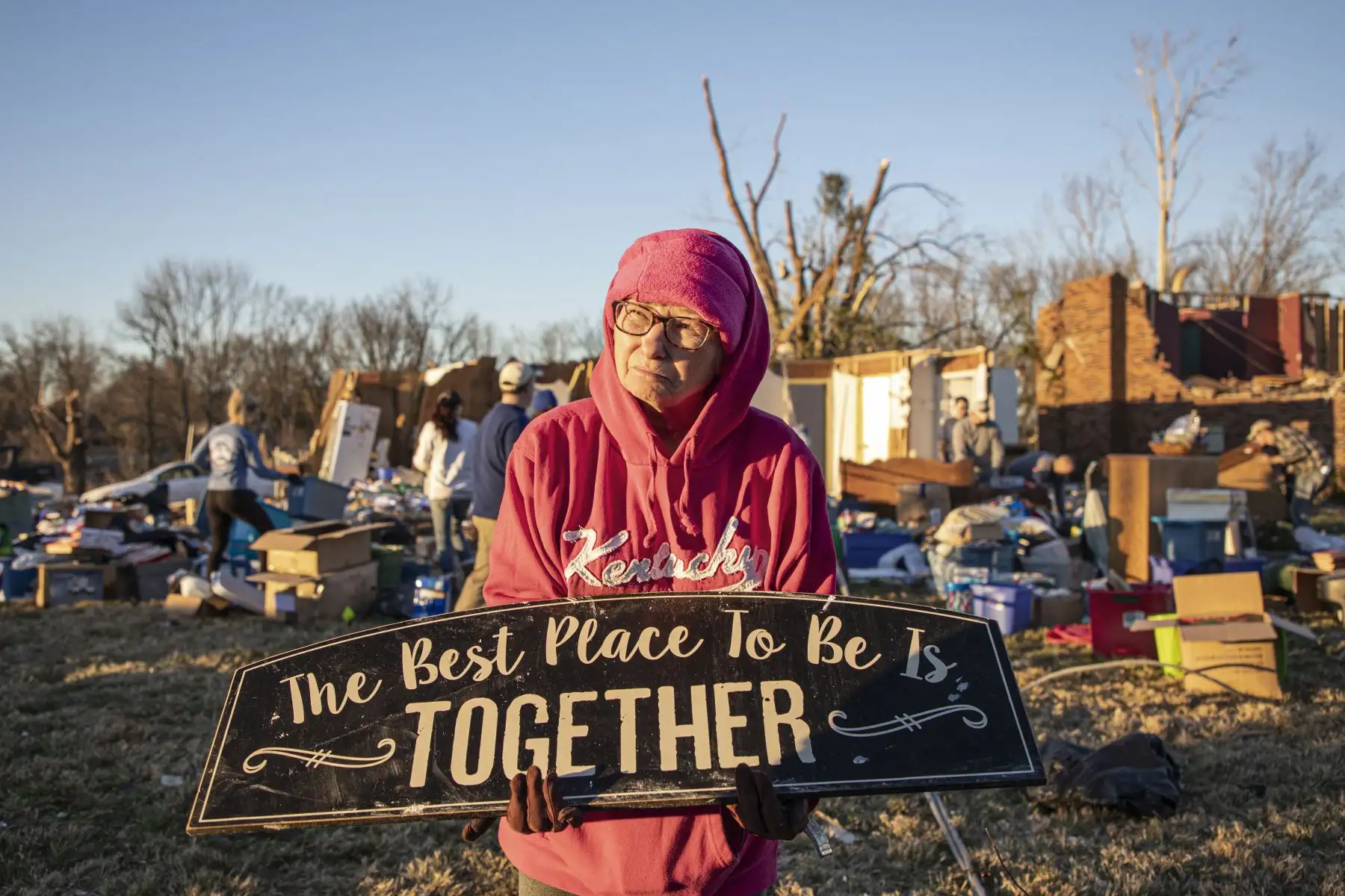 Kitty Williams sostiene un letrero que sobrevivió a la tormenta mientras sus amigos y familiares la ayudan a recoger sus pertenencias de lo que queda de su casa después de que el clima extremo azotara el área, en Bowling Green, Kentucky, el 13 de diciembre de 2021. Foto: AFP