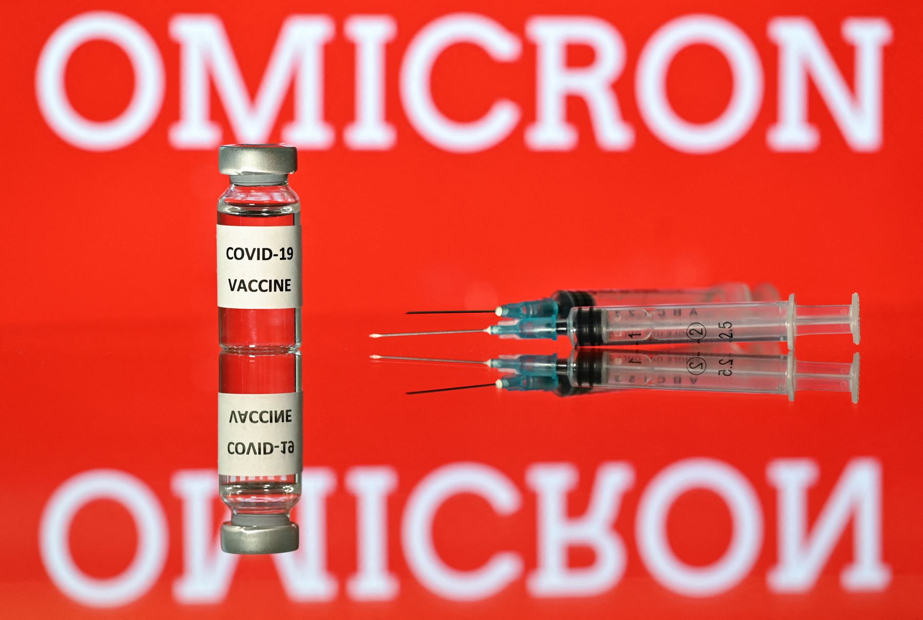 Una imagen de ilustración tomada en Londres el 2 de diciembre del 2021 muestra jeringa y una pantalla que muestra la palabra ómicron, el nombre de la nueva variante del covid-19, y una ilustración del virus. Foto: Justin TALLIS/AFP