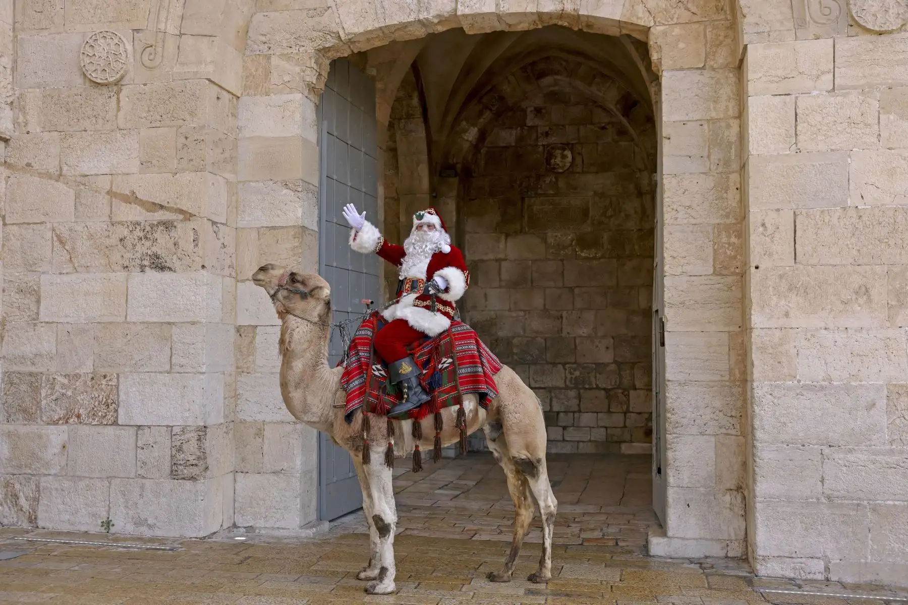 Un palestino vestido como Papá Noel hace gestos mientras monta un camello en la Ciudad Vieja de Jerusalén durante las celebraciones navideñas. Foto:  AFP