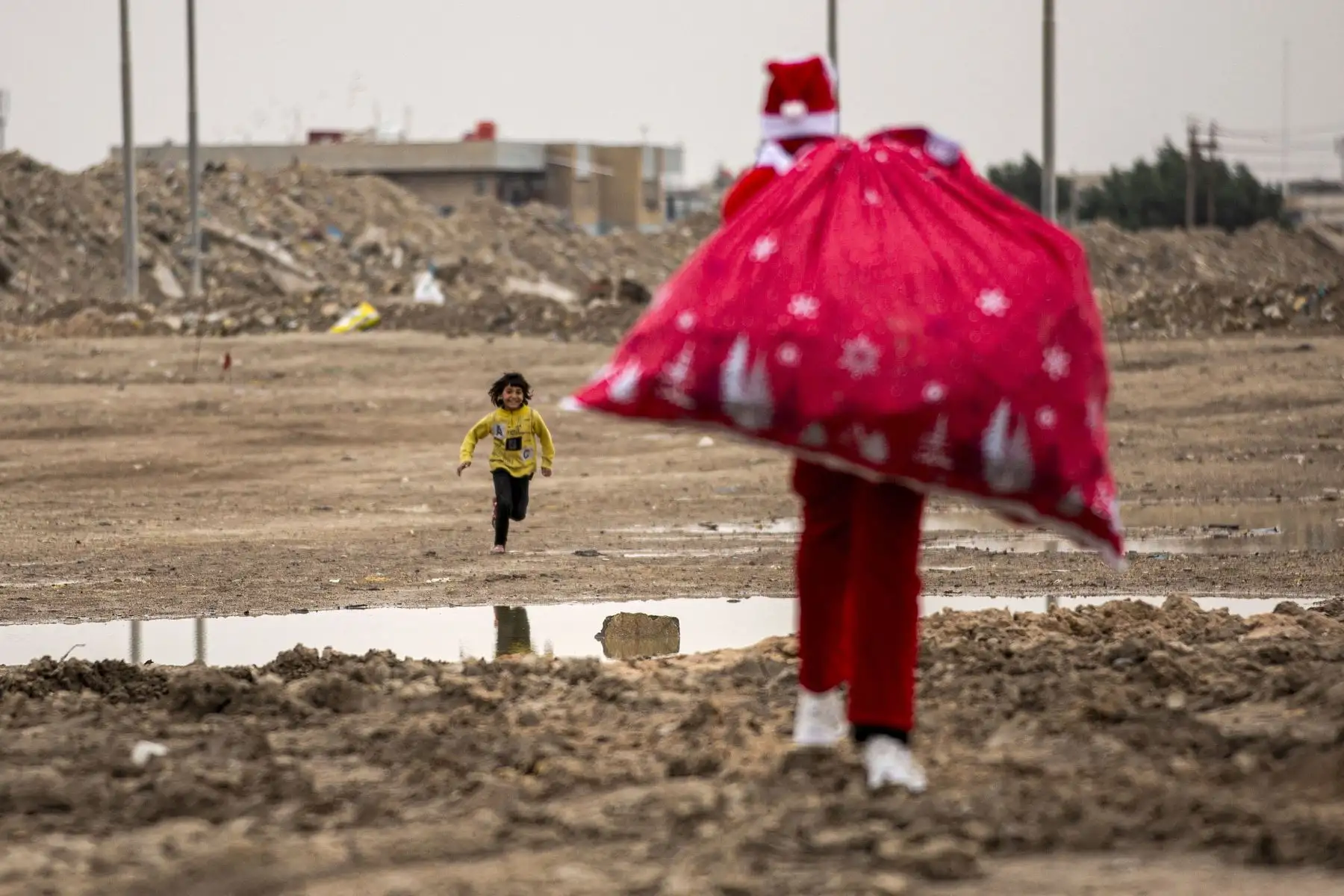Un niño corre hacia Mohamed Maarouf, de 28 años, mientras camina con un saco de regalos vestido con el traje de San Nicolás (Papá Noel) en un barrio pobre cerca del centro de la ciudad de Basora, en el sur de Irak, el 25 de diciembre de 2021.Foto: AFP