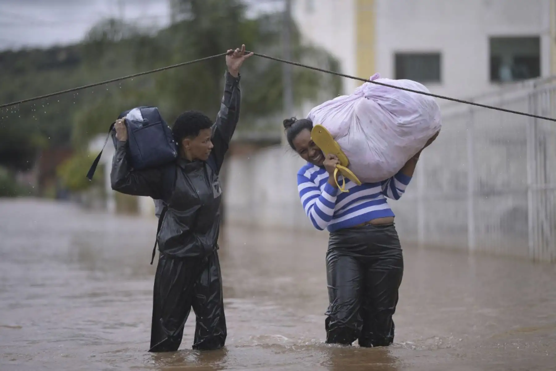 Personas cruzan una calle inundada llevando sus pertenencias a causa de las inundaciones en el municipio brasileño de Juatuba, ubicado en el estado de Minas Gerais, el 10 de enero de 2022, luego de que en los últimos días cayeran lluvias torrenciales en la parte sureste del país. país. Foto: AFP