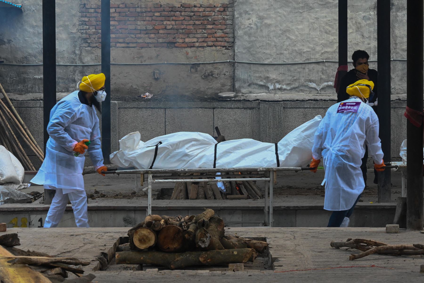 Voluntarios en equipo de protección personal llevan en una camilla el cuerpo de una persona que murió a causa del coronavirus Covid-19, en un crematorio en Nueva Delhi. Foto: AFP