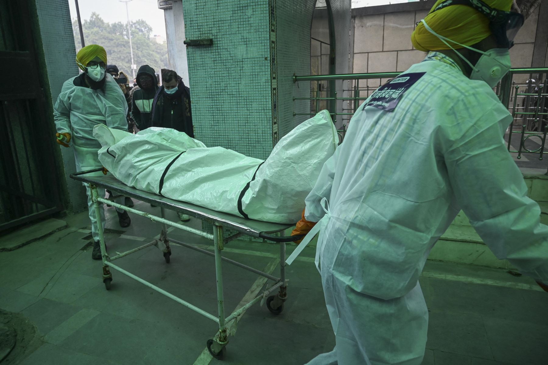 Voluntarios en equipo de protección personal (EPP) llevan el cuerpo de una persona que murió a causa del coronavirus Covid-19, en un crematorio en Nueva Delhi, Foto: AFP
