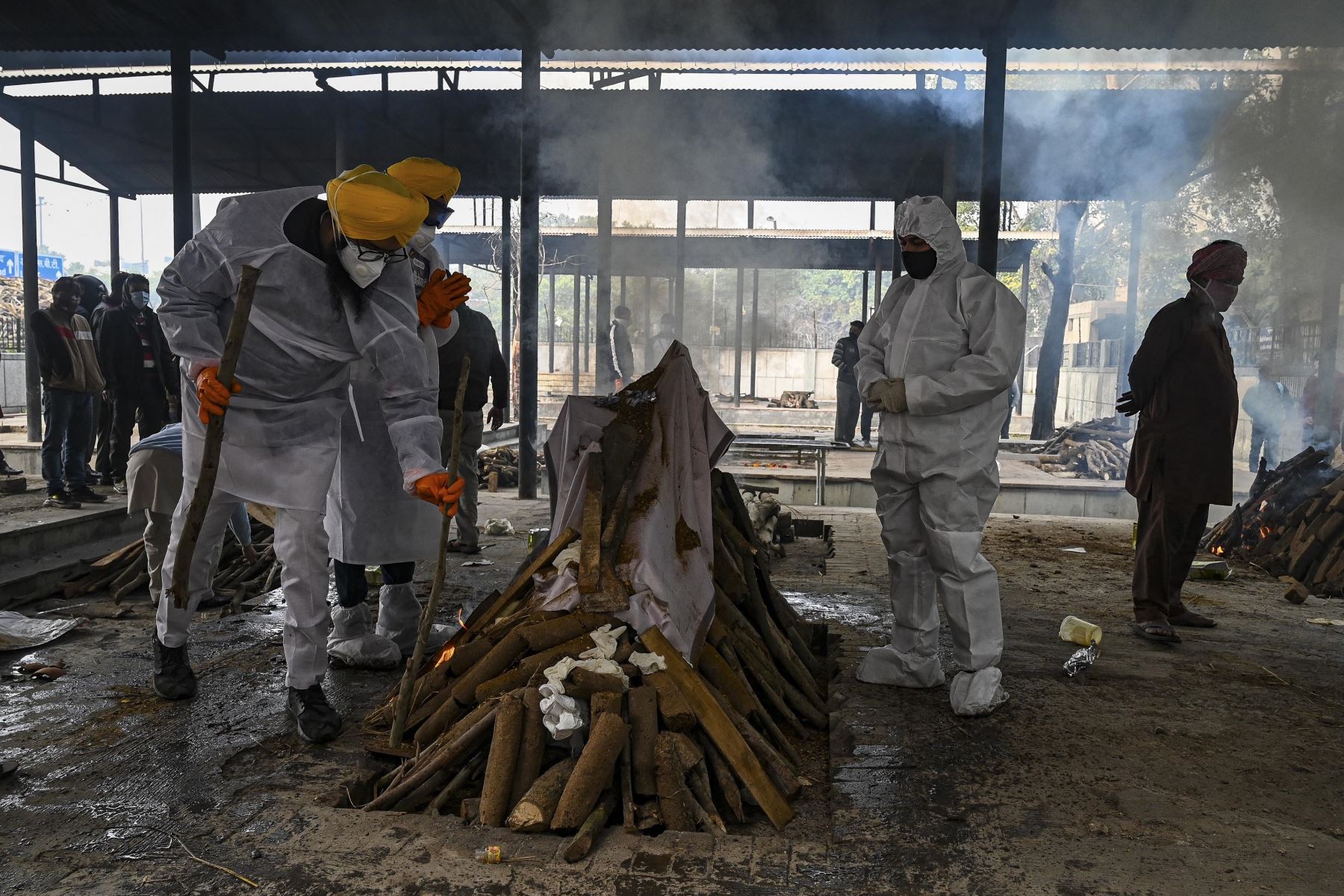 Voluntarios en trajes de equipo de protección personal y familiares realizan los últimos ritos durante la cremación de una persona que murió debido al coronavirus Covid-19, en un crematorio en Nueva Delhi. Foto: AFP