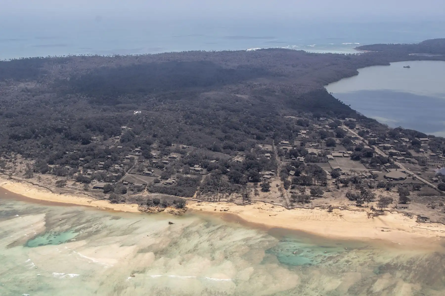 Una foto proporcionada por la Fuerza de Defensa de Nueva Zelanda (NZDF) muestra una vista aérea de un avión P-3K2 Orion mientras vuela sobre una fuerte caída de ceniza en un área de Tonga el 17 de enero de 2022 (emitido el 18 de enero de 2022), con ceniza en los techos de las casas y la vegetación circundante. Foto: EFE