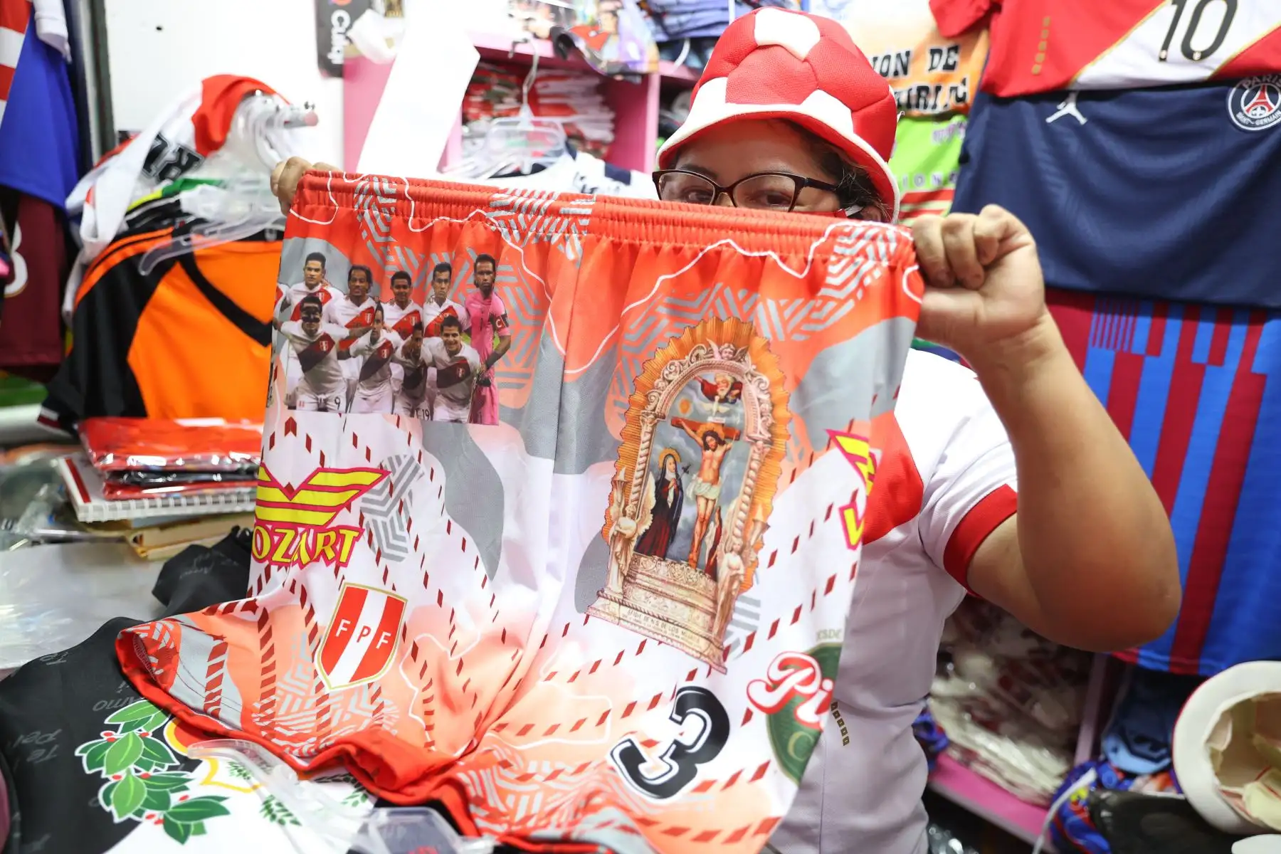 Todo vale para cerrar una venta: una comerciante muestra un short multicolor con imágenes de la selección peruana de fútbol, el Señor de los Milagros y una conocida cerveza local, a 24 horas del partido Perú-Ecuador que puede colocar a la selección blanquirroja a medio paso de Catar 2022. En el emporio textil de Gamarra se ofertan camisetas desde 10 soles para adultos, las que pueden personalizarse por uno o dos soles adicionales. Foto: ANDINA/Jhonel Rodríguez