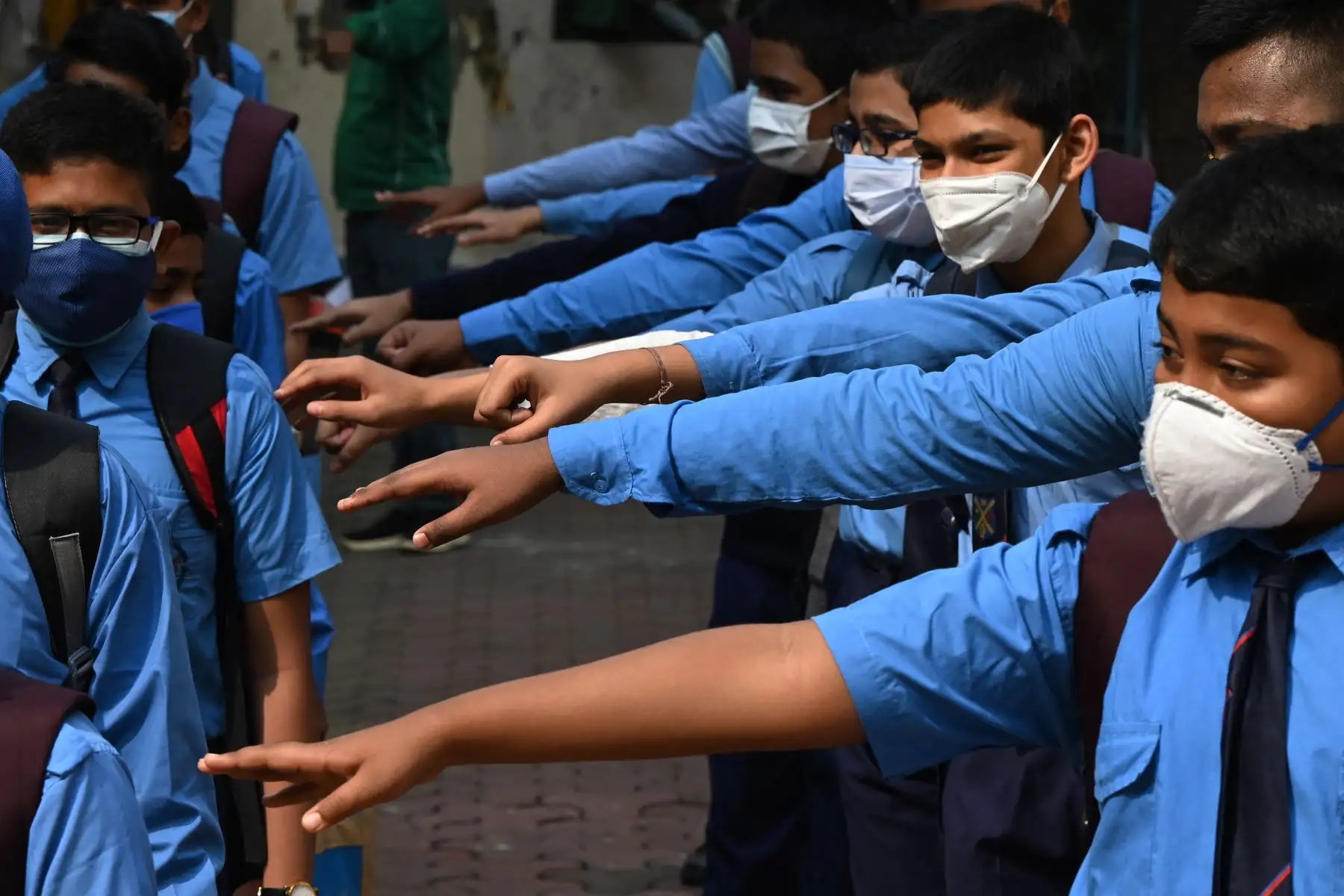 Los niños estiran los brazos para observar el distanciamiento social, que es uno de los protocolos de seguridad del coronavirus Covid-19, en un colegio en la India. Foto: AFP