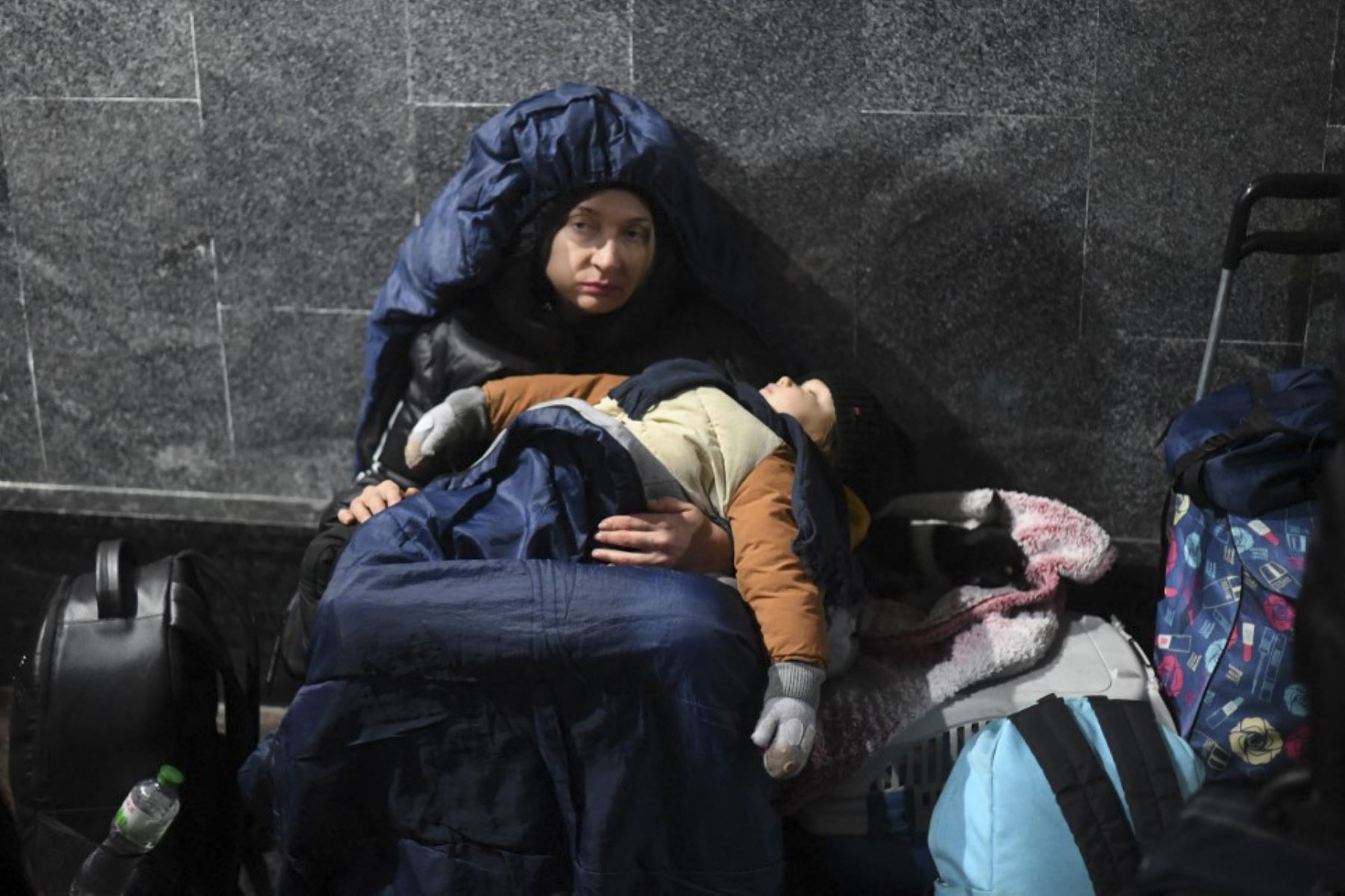 Una mujer sostiene a su hijo dormido mientras está sentada en el suelo en la estación central de trenes de Lviv, en el oeste de Ucrania. Foto: AFP