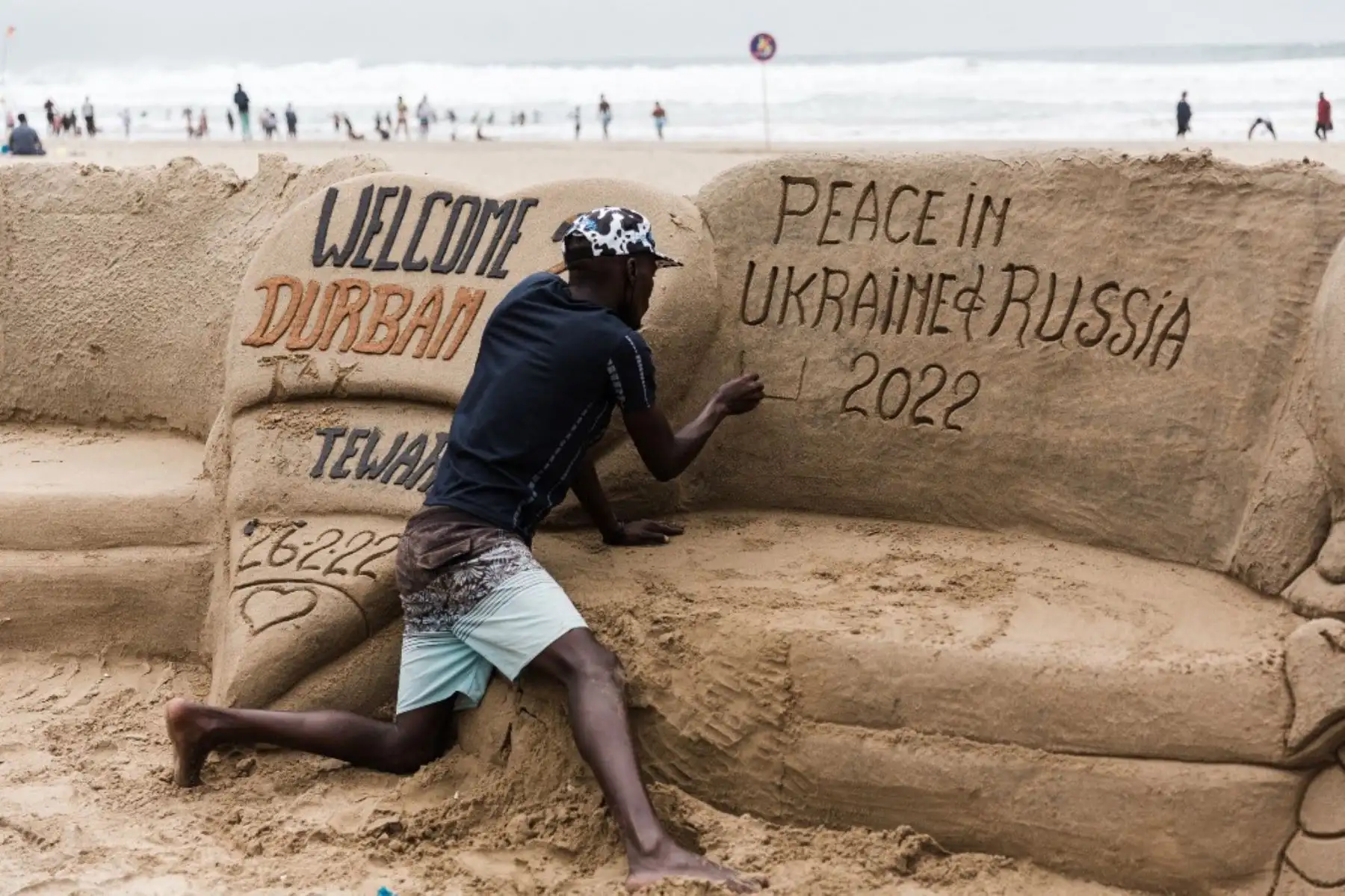 El escultor de arena sudafricano Sithembiso Buthelezi da los toques finales mostrando un mensaje que llama a la paz entre Ucrania y Rusia en la playa norte de Durban, el 27 de febrero de 2022. Foto: AFP