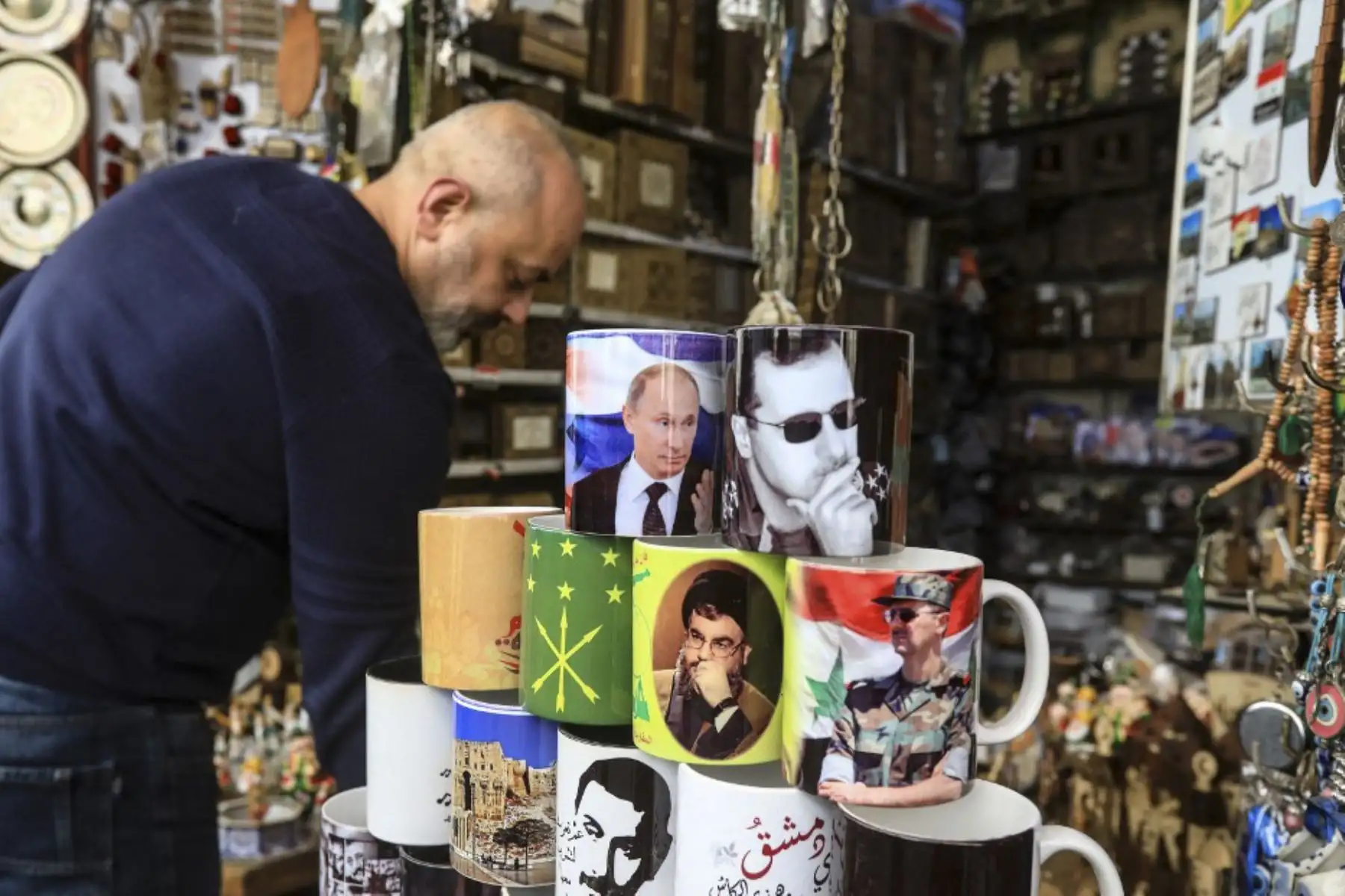 El propietario de una tienda de souvenirs muestra objetos con imágenes del presidente sirio Bashar al-Assad, el presidente ruso Vladimir Putin y el jefe del movimiento chiíta libanés Hezbollah Hassan Nasrallah, en la antigua Damasco, el 27 de febrero de 2022. Foto: AFP
