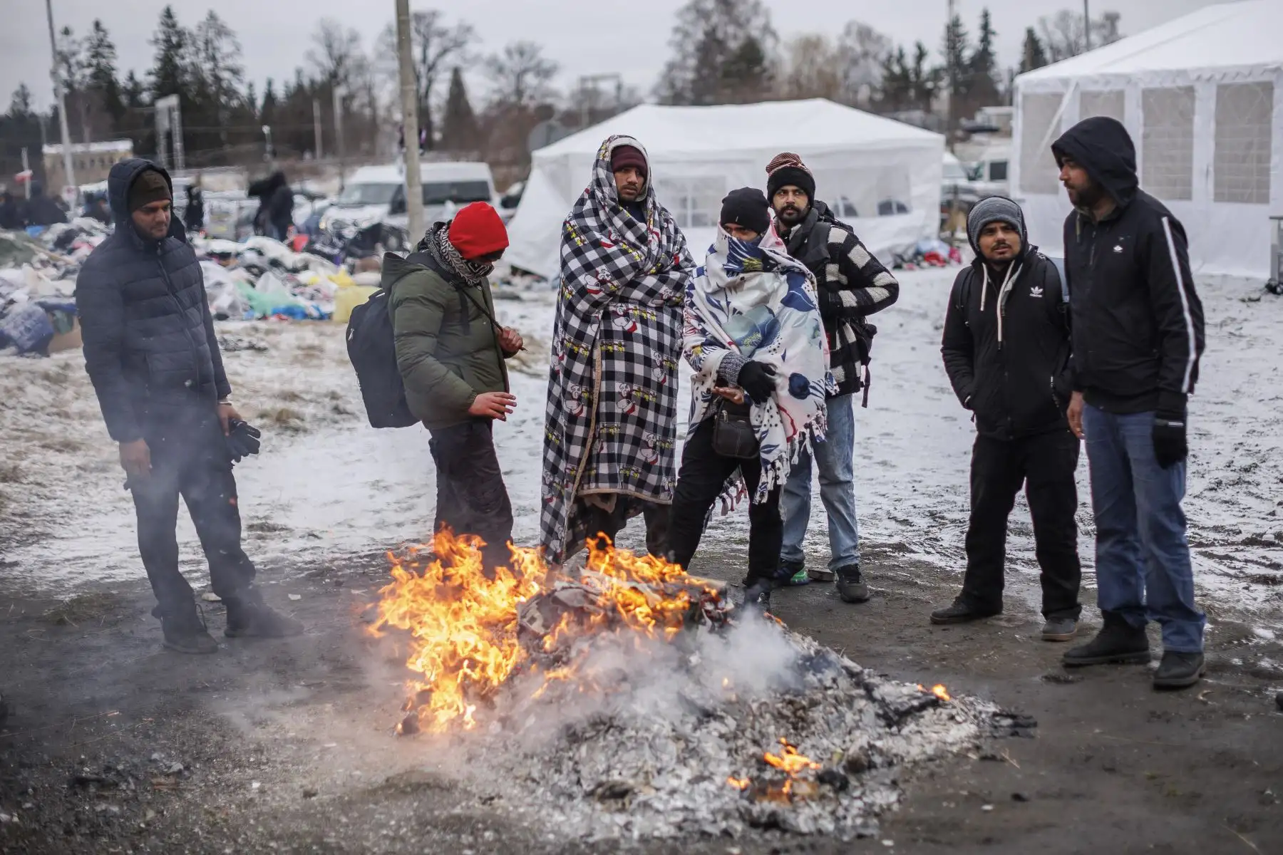 Varias personas procedentes de Ucrania tratan de combatir el frío tras cruzar la frontera con Polonia huyendo de la guerra. Foto: EFE