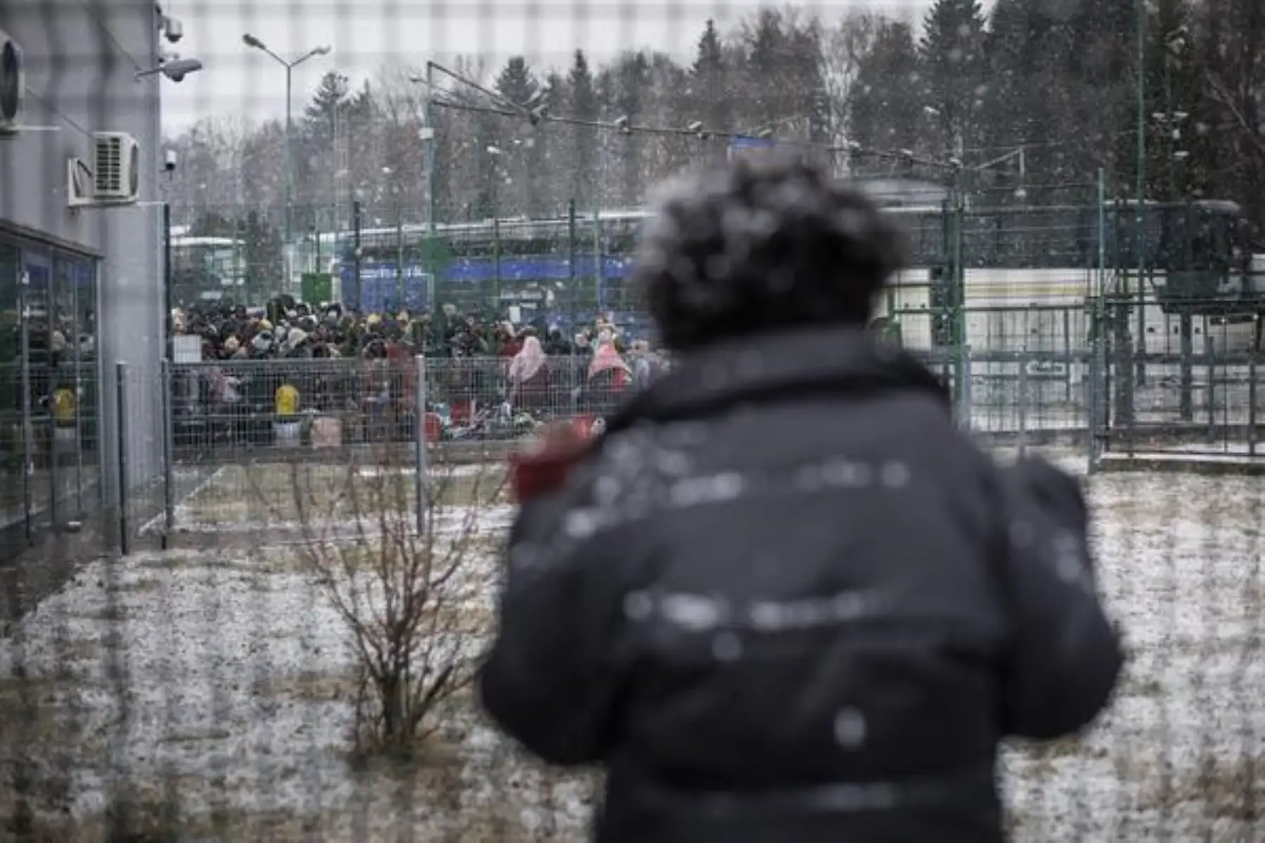 Una persona procedente de Ucrania huyendo de la guerra, observa a varias personas retenidas en la parte polaca de la frontera. Foto: EFE