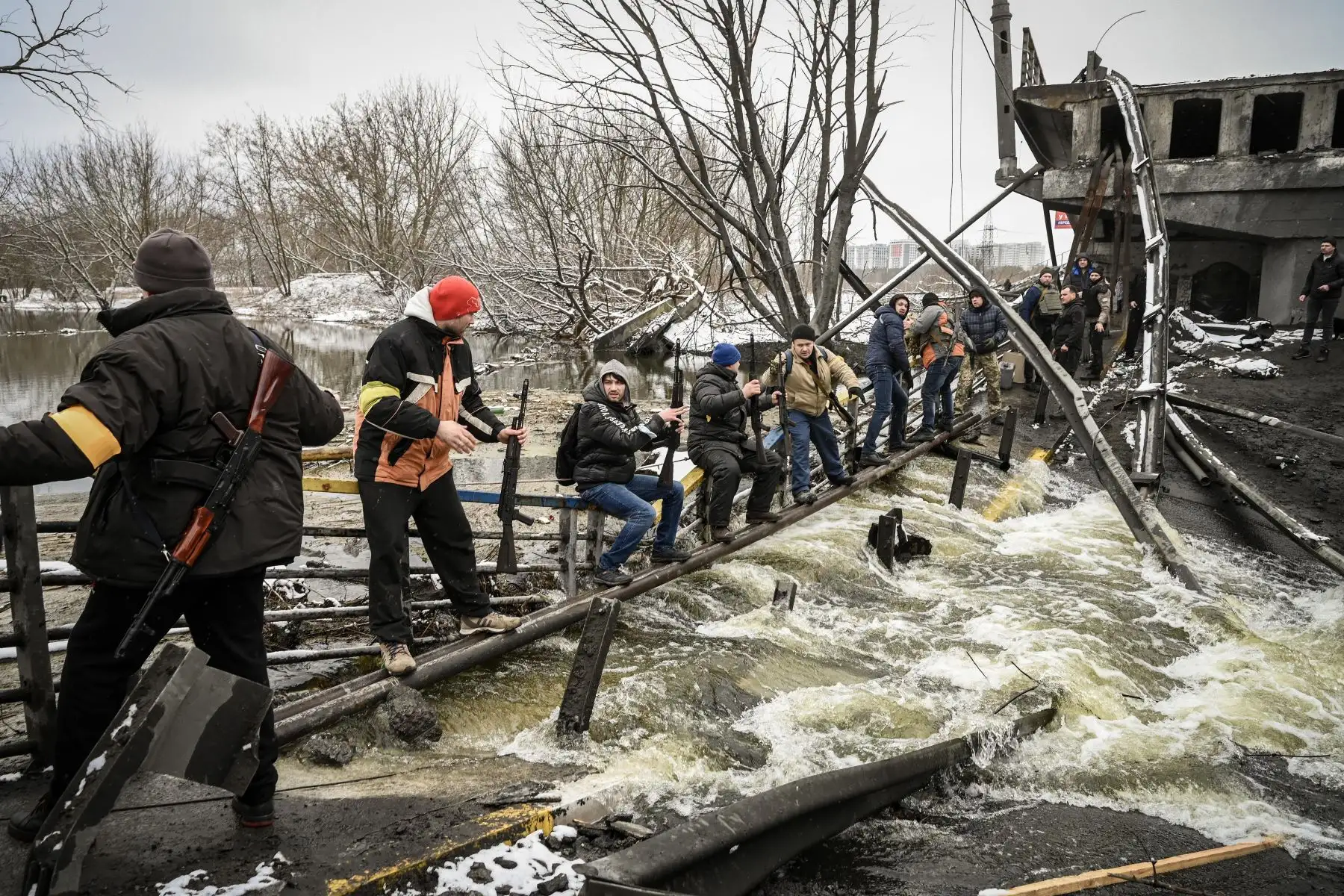 Miembros de una unidad de defensa civil ucraniana pasan nuevos rifles de asalto al lado opuesto de un puente volado en el frente norte de Kiev. Foto: AFP