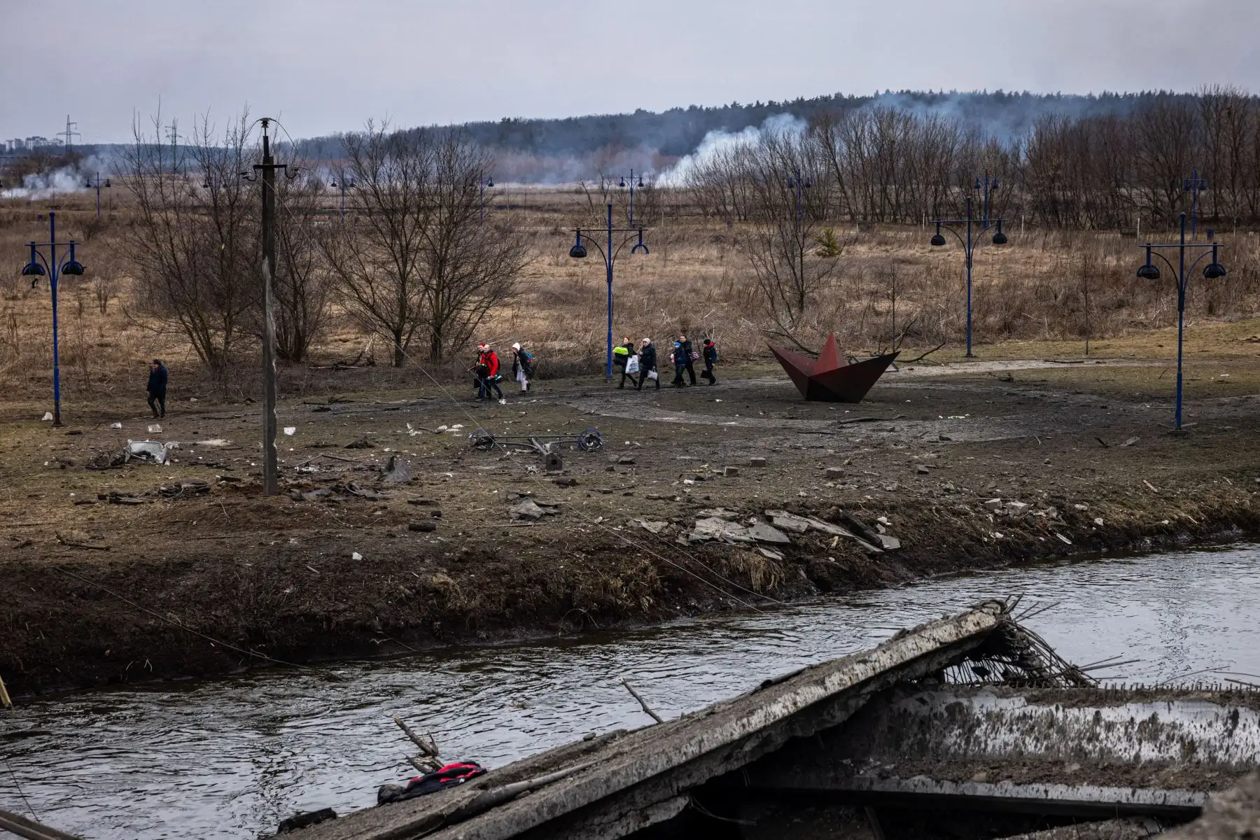 Ucranianos evacuados  caminan a lo largo de la orilla del río cerca de un puente destruido mientras huyen de la ciudad de Irpin, al noroeste de Kiev.
Foto: AFP