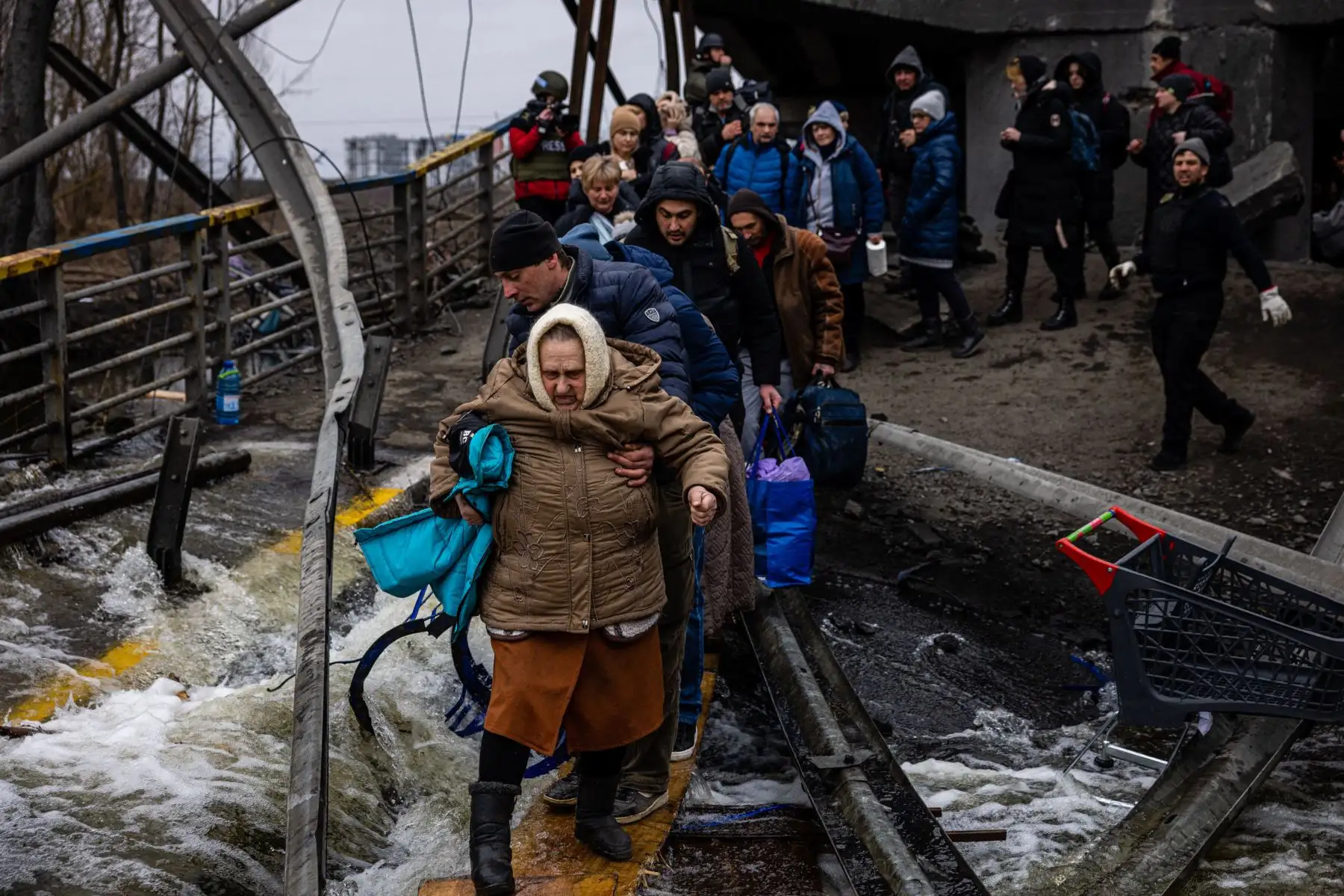 Un hombre ayuda a una mujer evacuada a cruzar un puente destruido mientras ella y otras personas huyen de la ciudad de Irpin, al noroeste de Kiev.
Foto: AFP