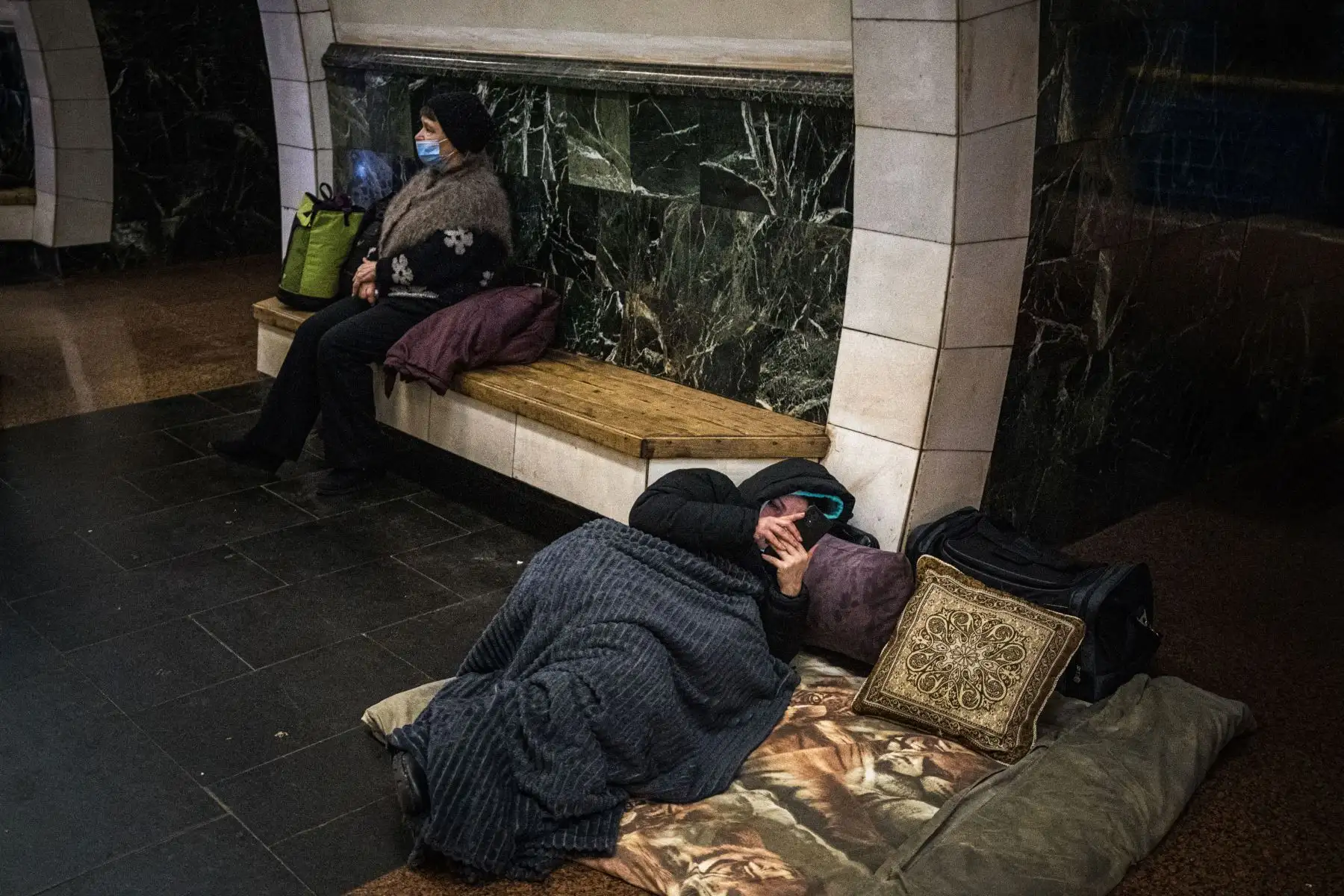 Una mujer revisa su teléfono inteligente acostada en una cama improvisada en una estación de metro subterránea utilizada como refugio antibombas en Kiev.
Foto: AFP