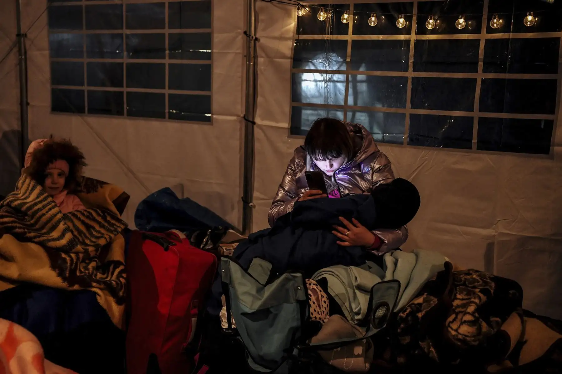 Una mujer que sostiene su pequeño mientras revisa su teléfono en una tienda de campaña después de cruzar la frontera de Ucrania con Polonia. Foto: AFP