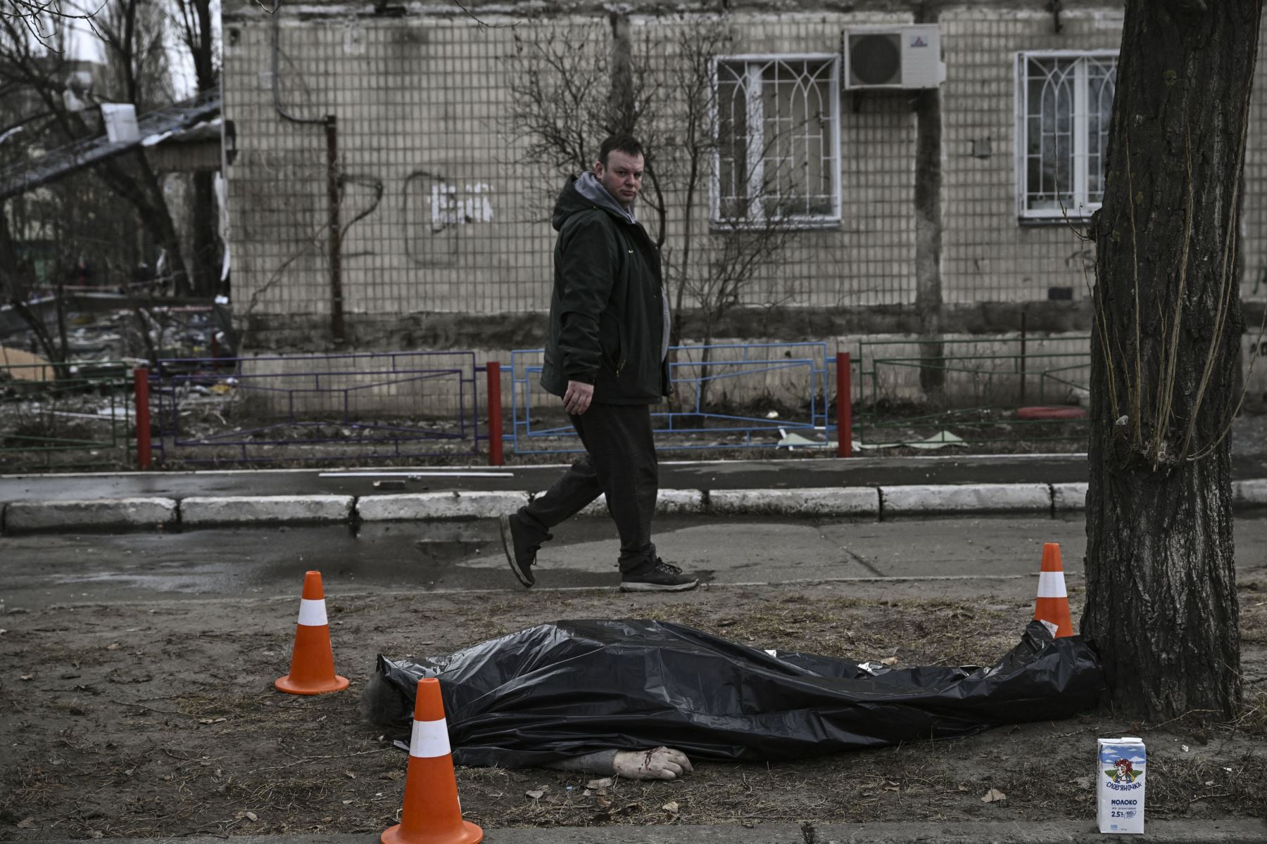 Un hombre pasa frente a un cuerpo cubierto que yace afuera de un bloque de apartamentos destruido después de que fue bombardeado en el distrito noroccidental de Obolon en Kiev.
Foto: AFP