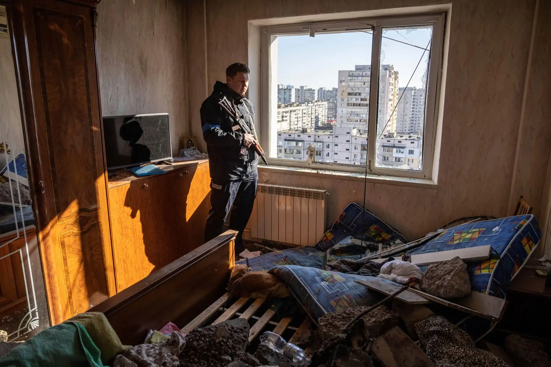Un oficial de policía mira a través de la ventana de un piso dañado en un edificio residencial que fue golpeado por los escombros de un cohete derribado en Kiev. Foto: AFP