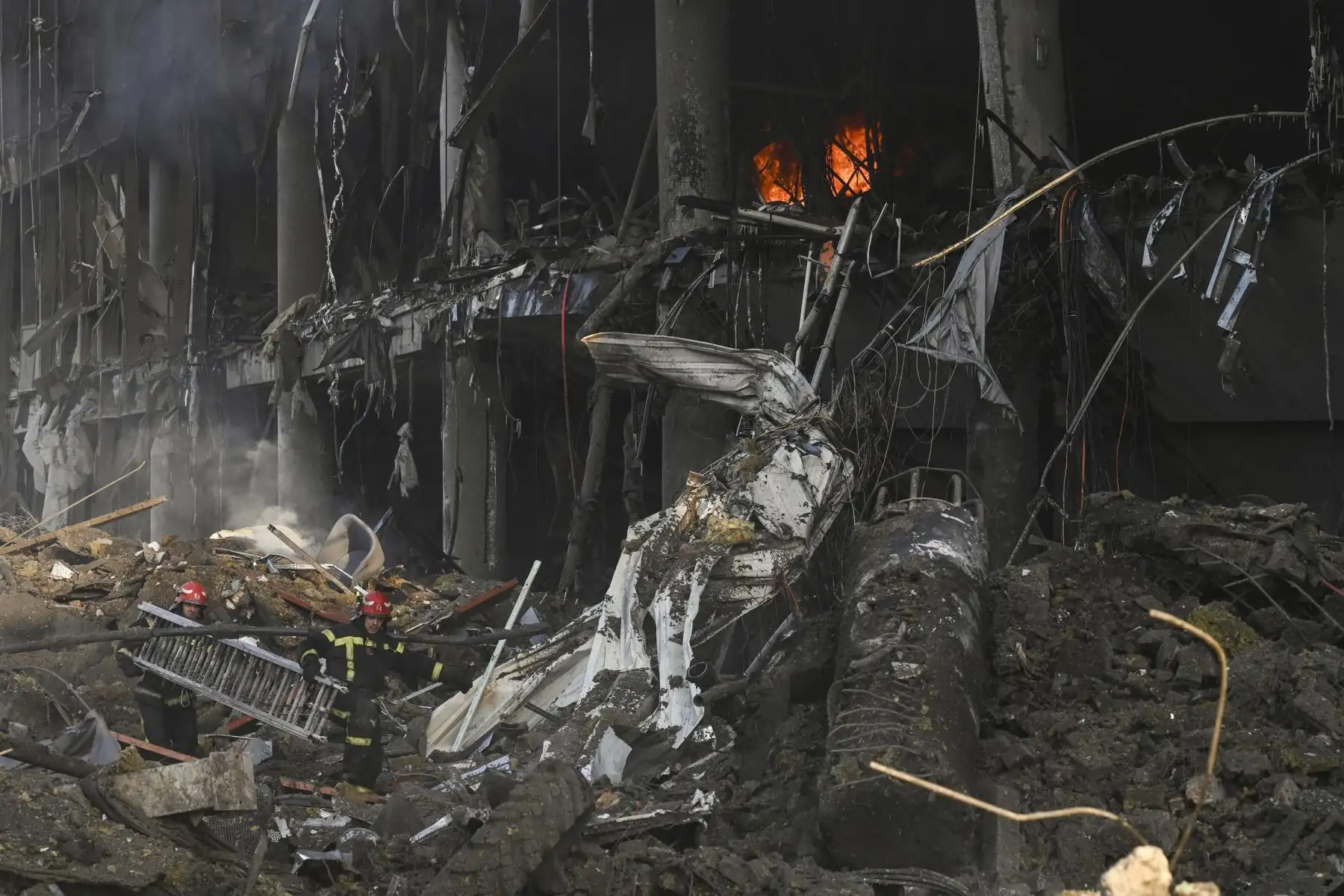 Bomberos llevan una escalera mientras avanzan entre los escombros tras los bombardeos rusos que destruyeron el centro comercial Retroville en Kiev. Foto: AFP