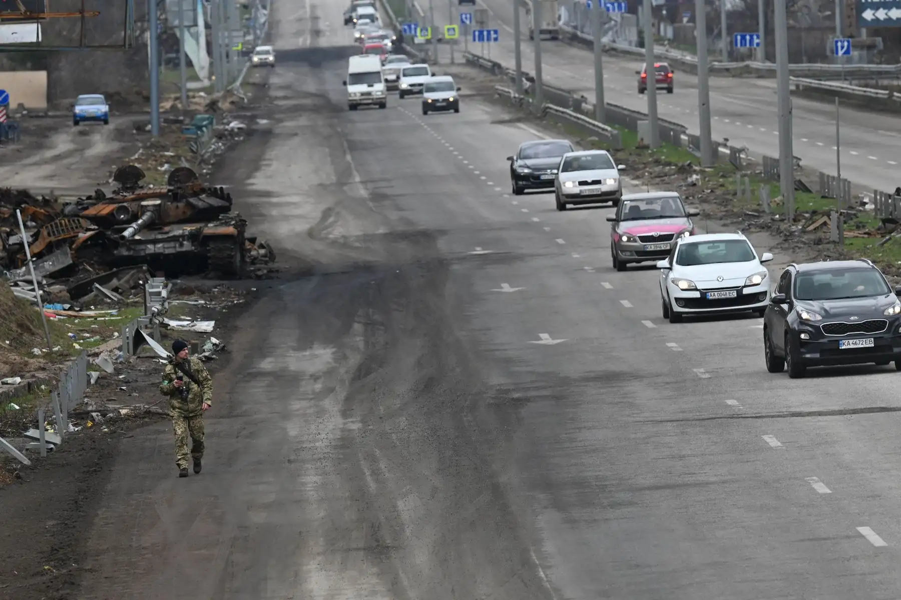 Un convoy de automóviles que evacuan a civiles pasa junto a un tanque ruso destruido en las afueras de la aldea de Buzova. Foto: AFP