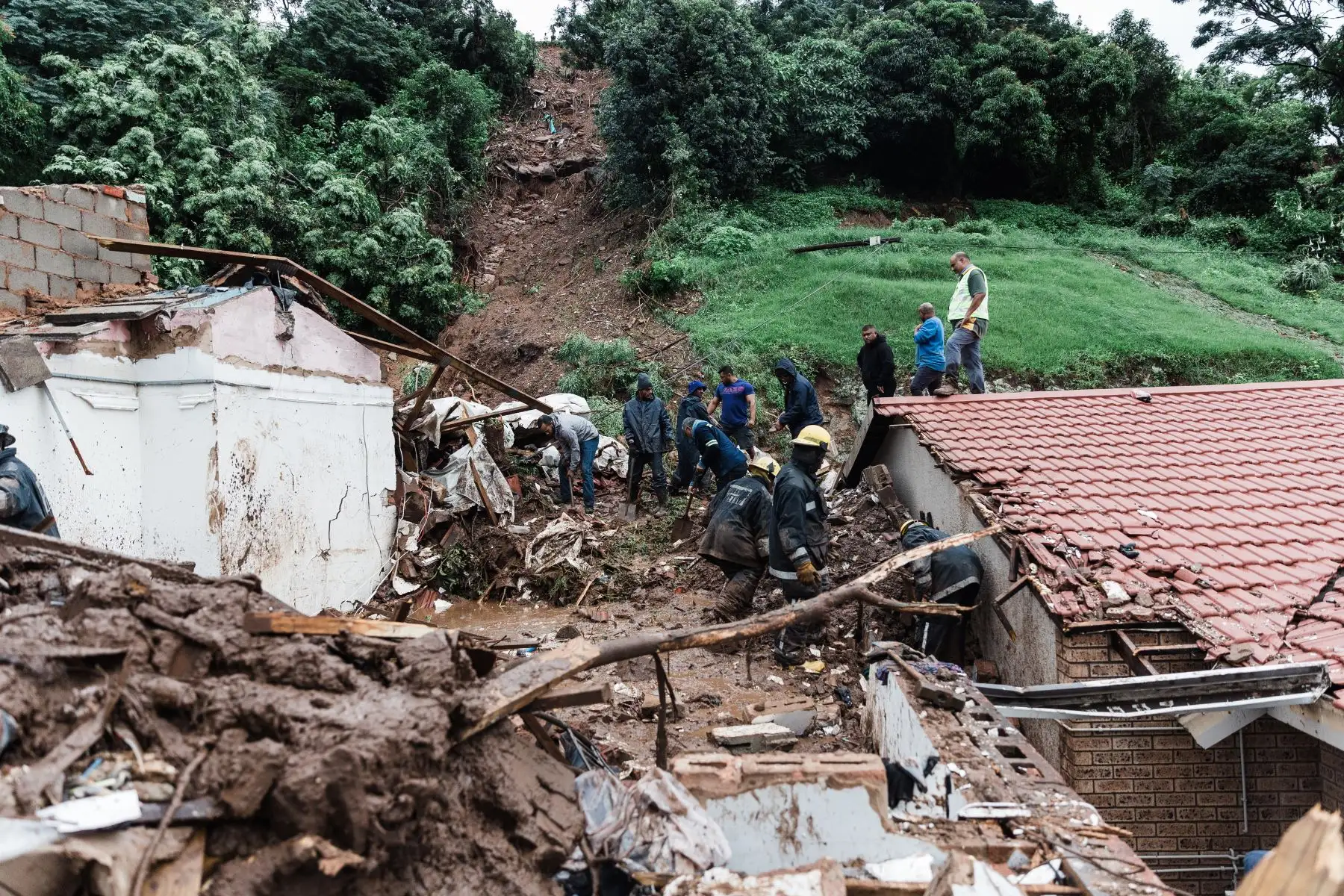 Los miembros del Departamento de Bomberos del Metro de Ethekwini y los residentes locales buscan a una persona que se cree que está atrapada después de que un deslizamiento de tierra en una casa en Durban se derrumbó luego de fuertes lluvias y vientos en Durban, el 12 de abril de 2022. 
Foto: ANDINA/AFP
