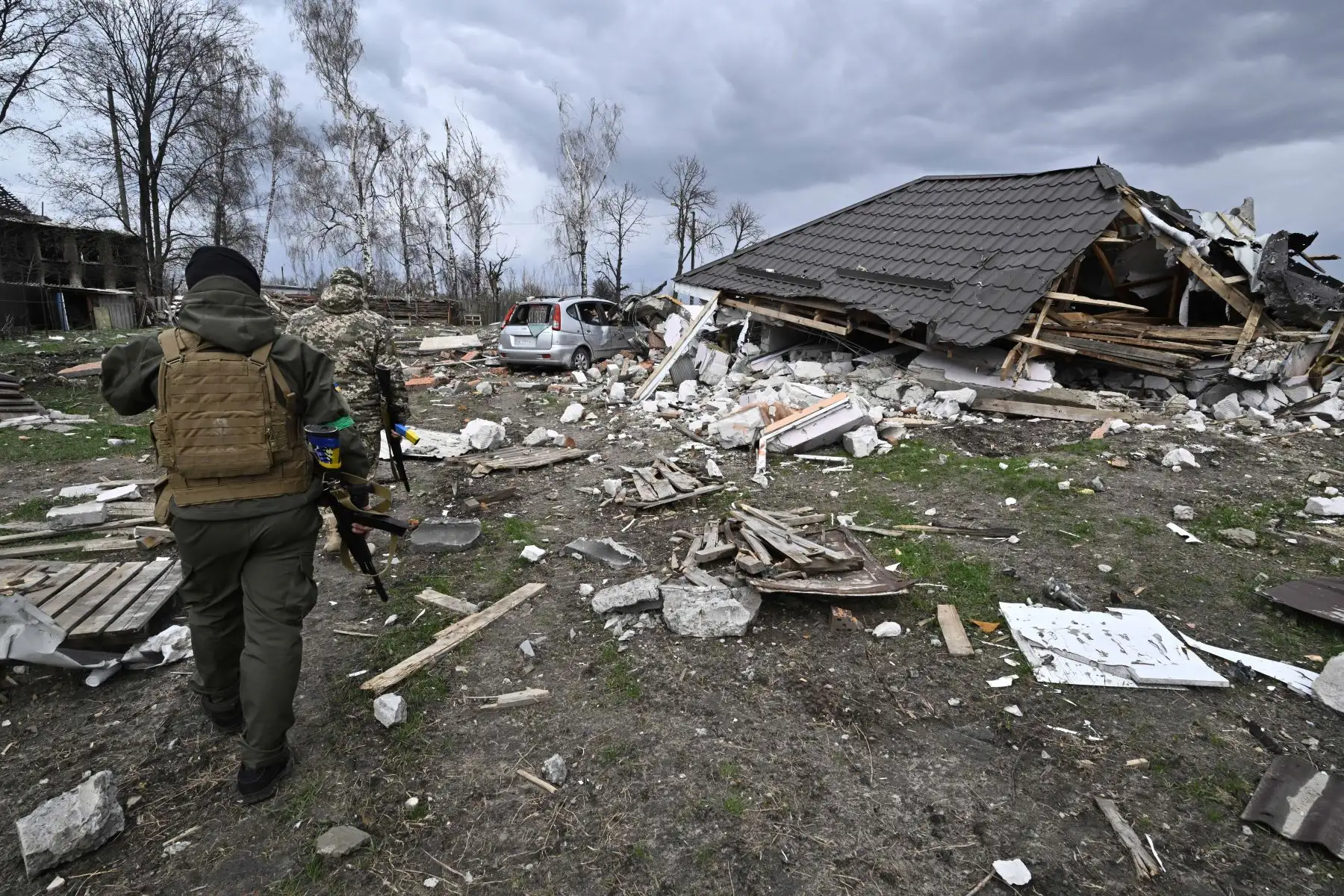 Miembros de las fuerzas de defensa territorial caminan frente a una casa destruida en la aldea de Bohdanivka, al noreste de Kiev. Foto: AFP