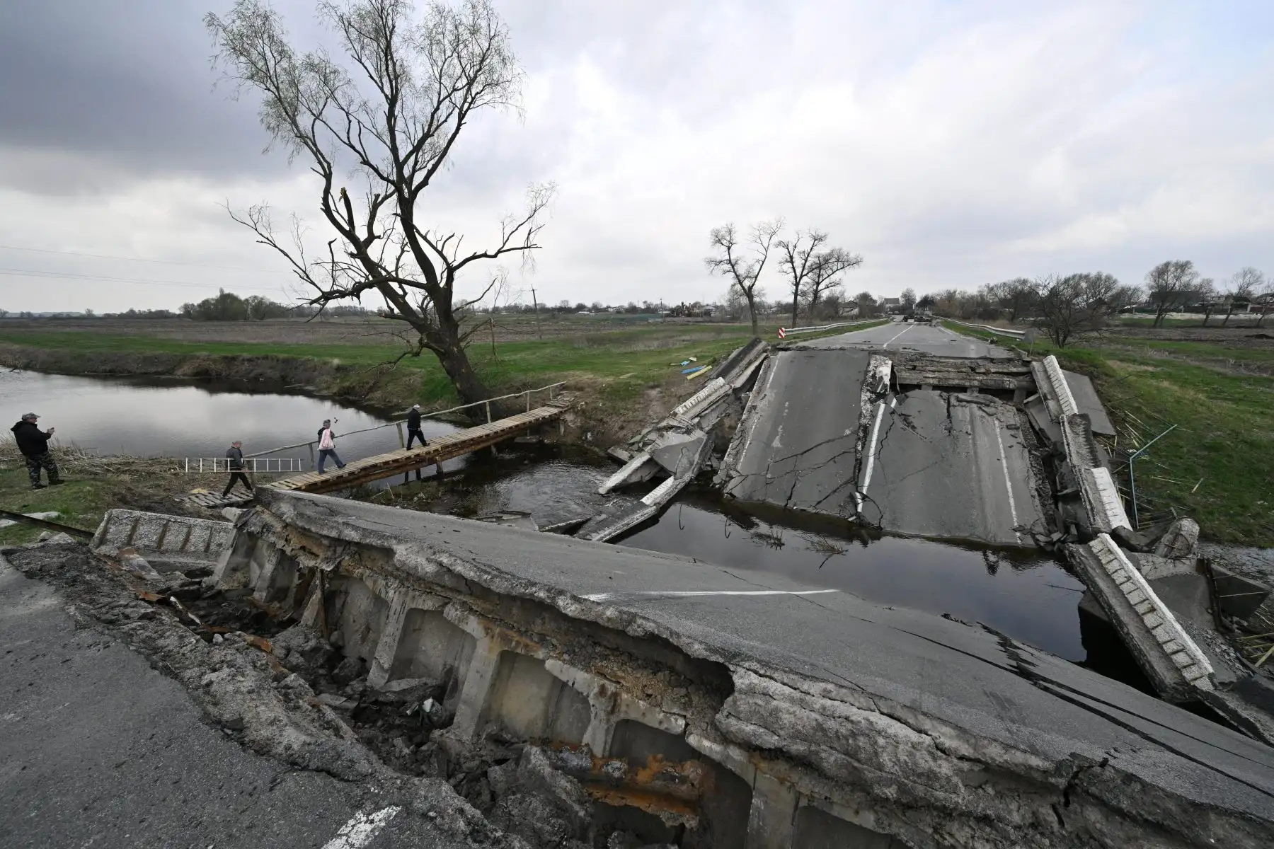 Residentes locales cruzan un río junto a un puente destruido en la aldea de Rusaniv, en la región de Kiev. Foto: AFP